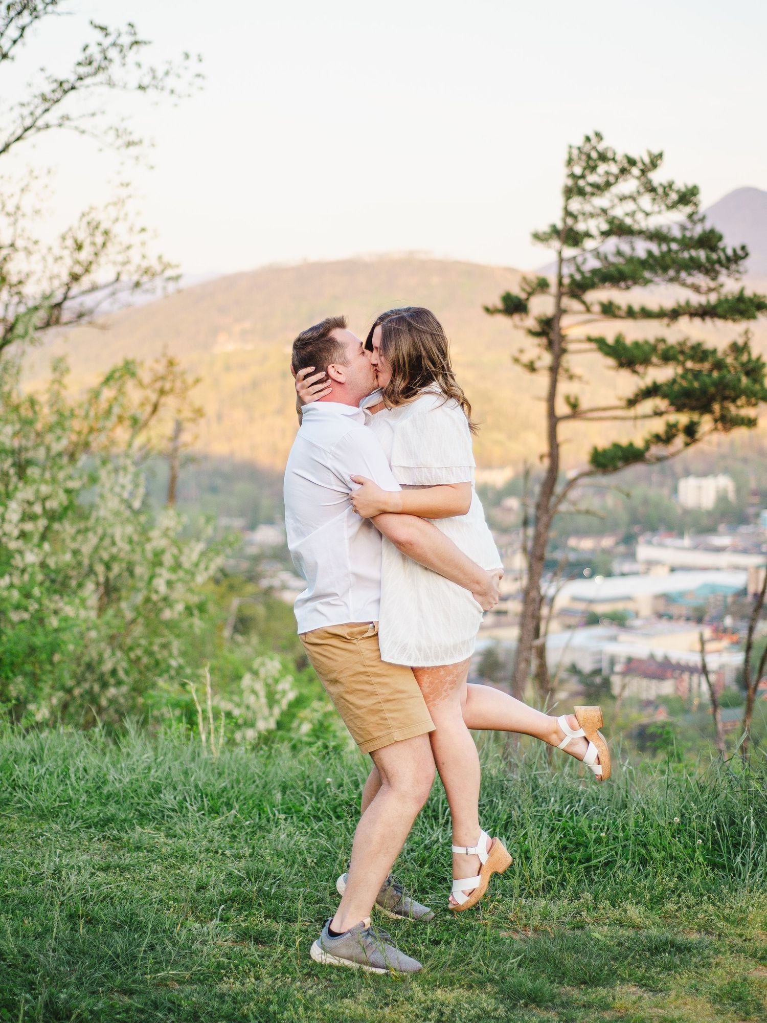 Couple sharing a romantic embrace on a hilltop overlooking a scenic valley during golden hour at the Gatlinburg scenic overlook.