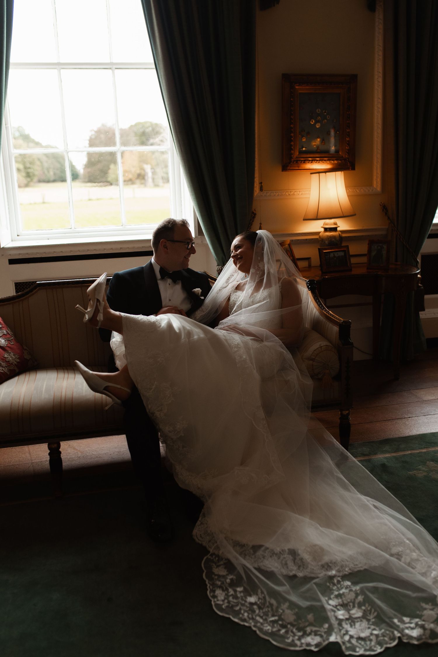 A flowing white wedding dress with delicate lace details is elegantly draped across a luxurious couch in a sunlit room.
