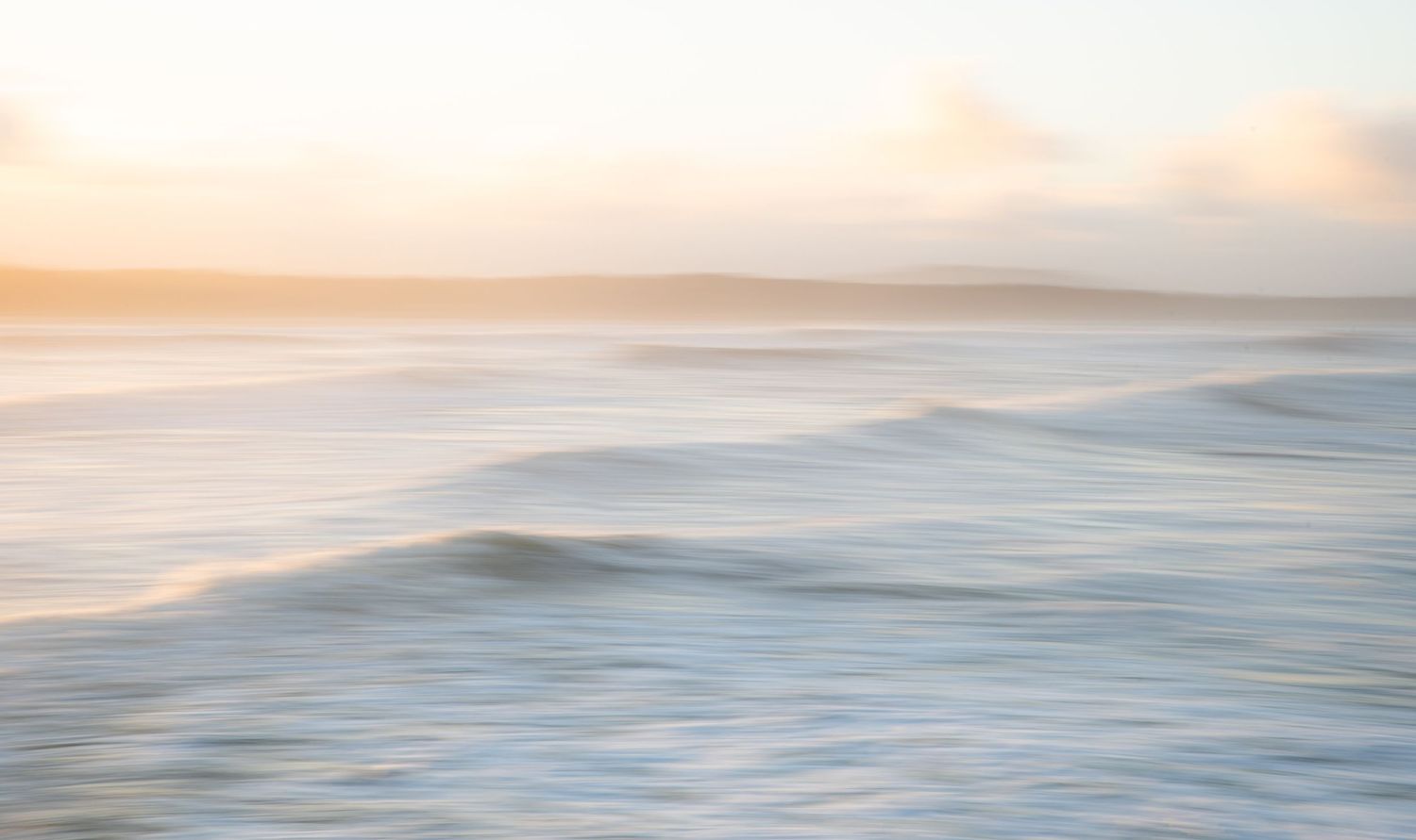 Tranquil ocean waves roll onto shore during a peaceful sunset with pastel colors in the sky.