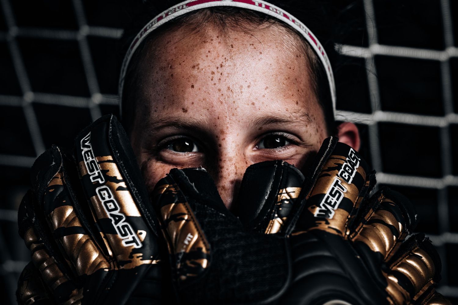 A young female goalkeeper from Crossfire Premier soccer club posing with her goalie gloves slightly covering her face.