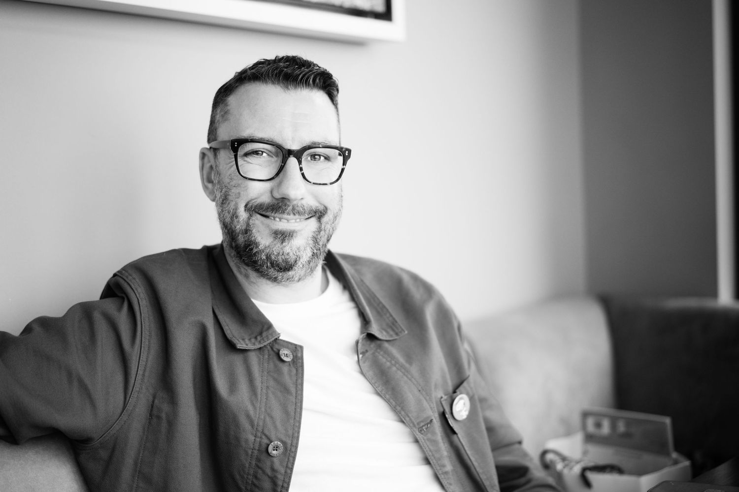 Black and white photo series showing a person wearing glasses and smiling in different poses against a light background.