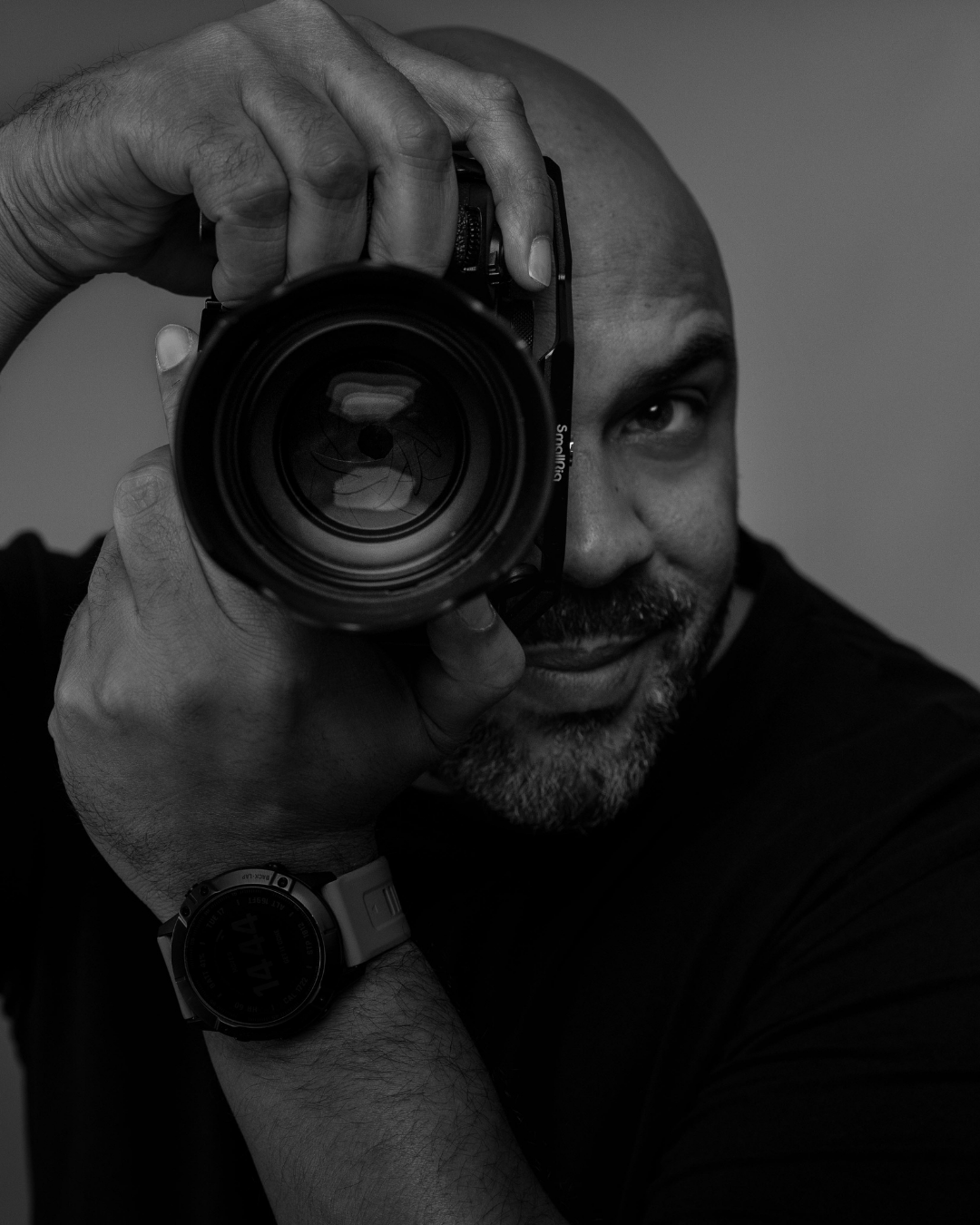 A dramatic black and white sequence showing a photographer holding a camera lens against a dark background.