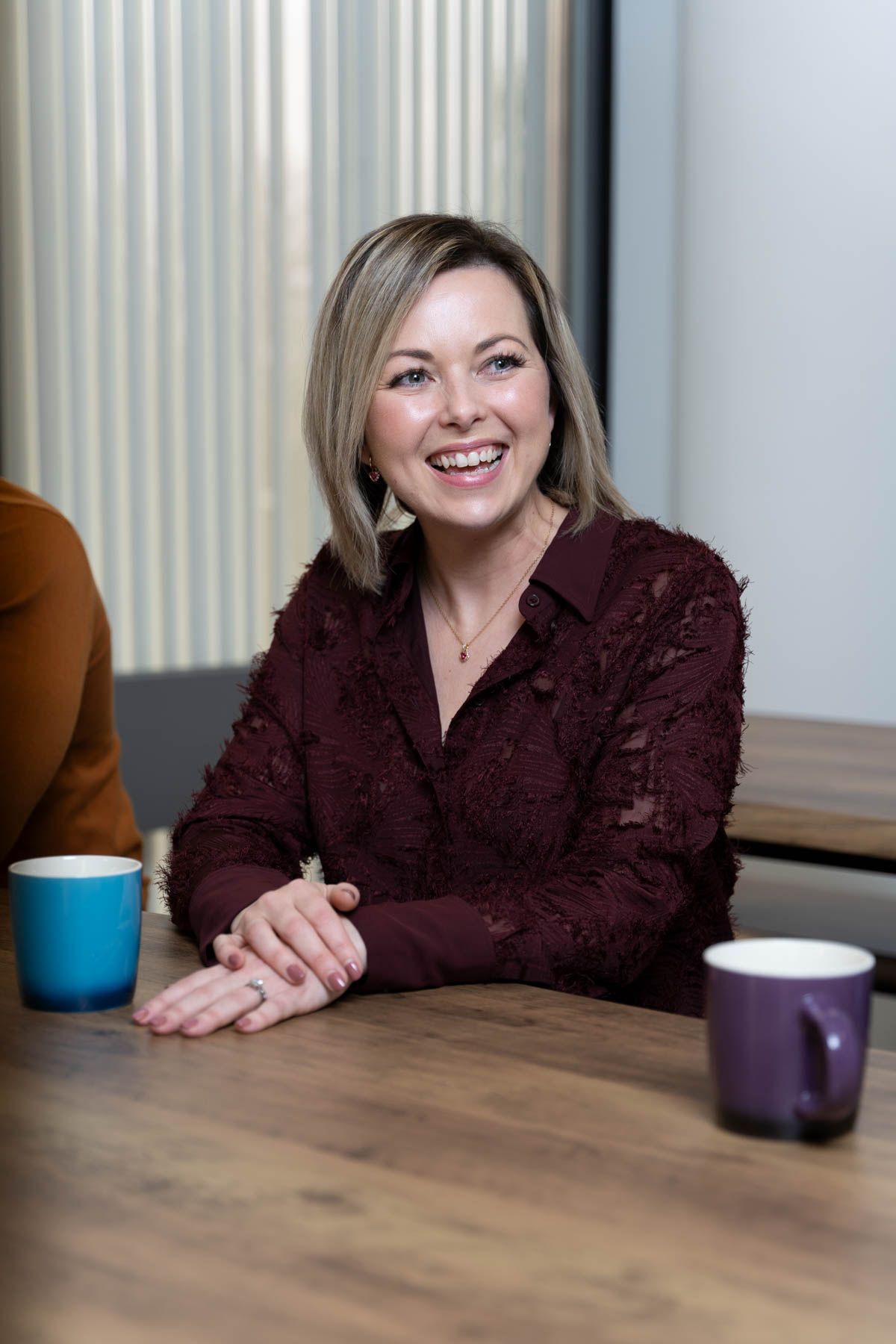 A person in a burgundy textured blouse sits at a wooden table with a coffee mug, shown in four sequential poses.