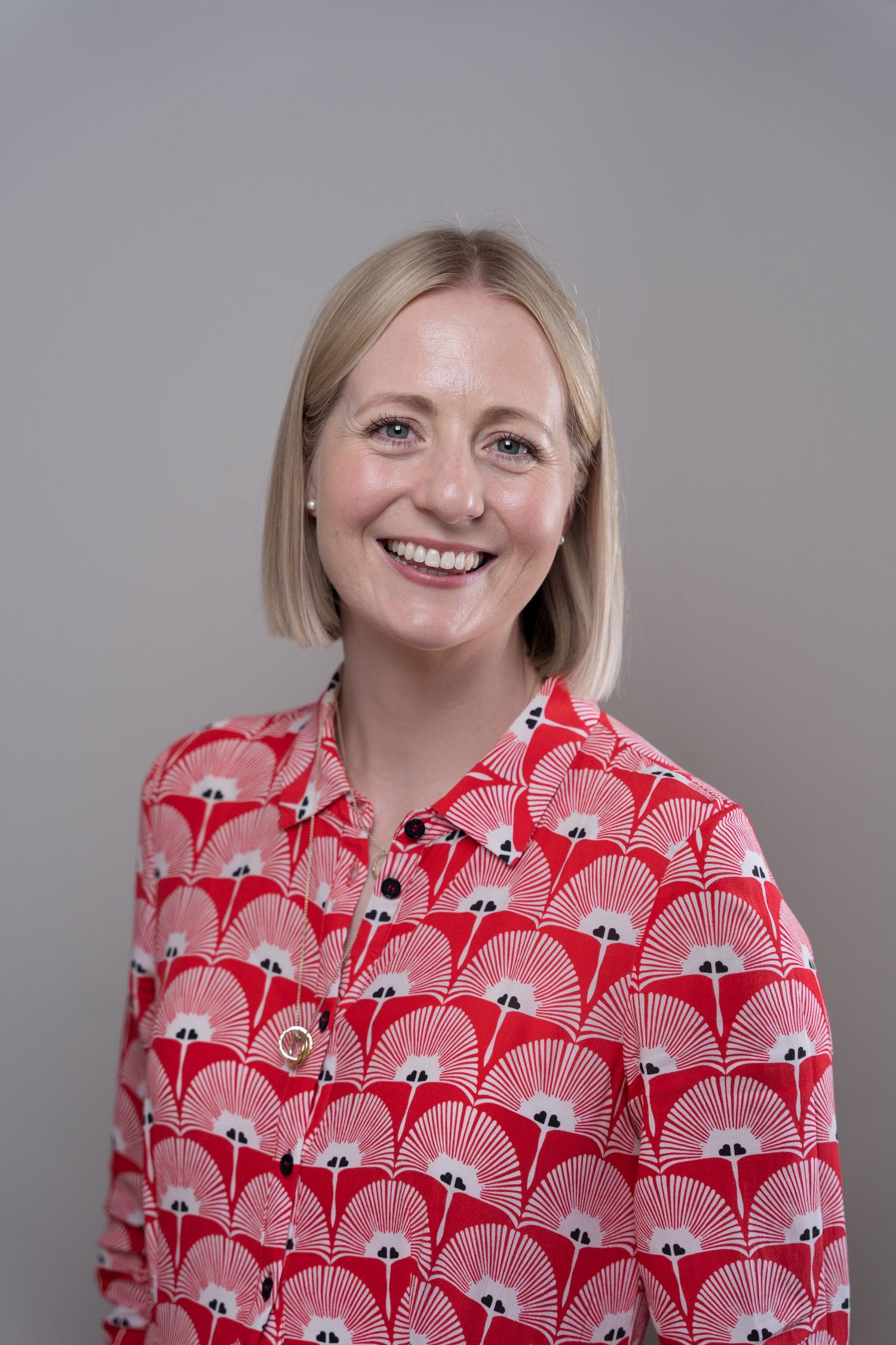 Woman wearing a vibrant red and white patterned blouse with fan-like designs smiles in a series of photos.