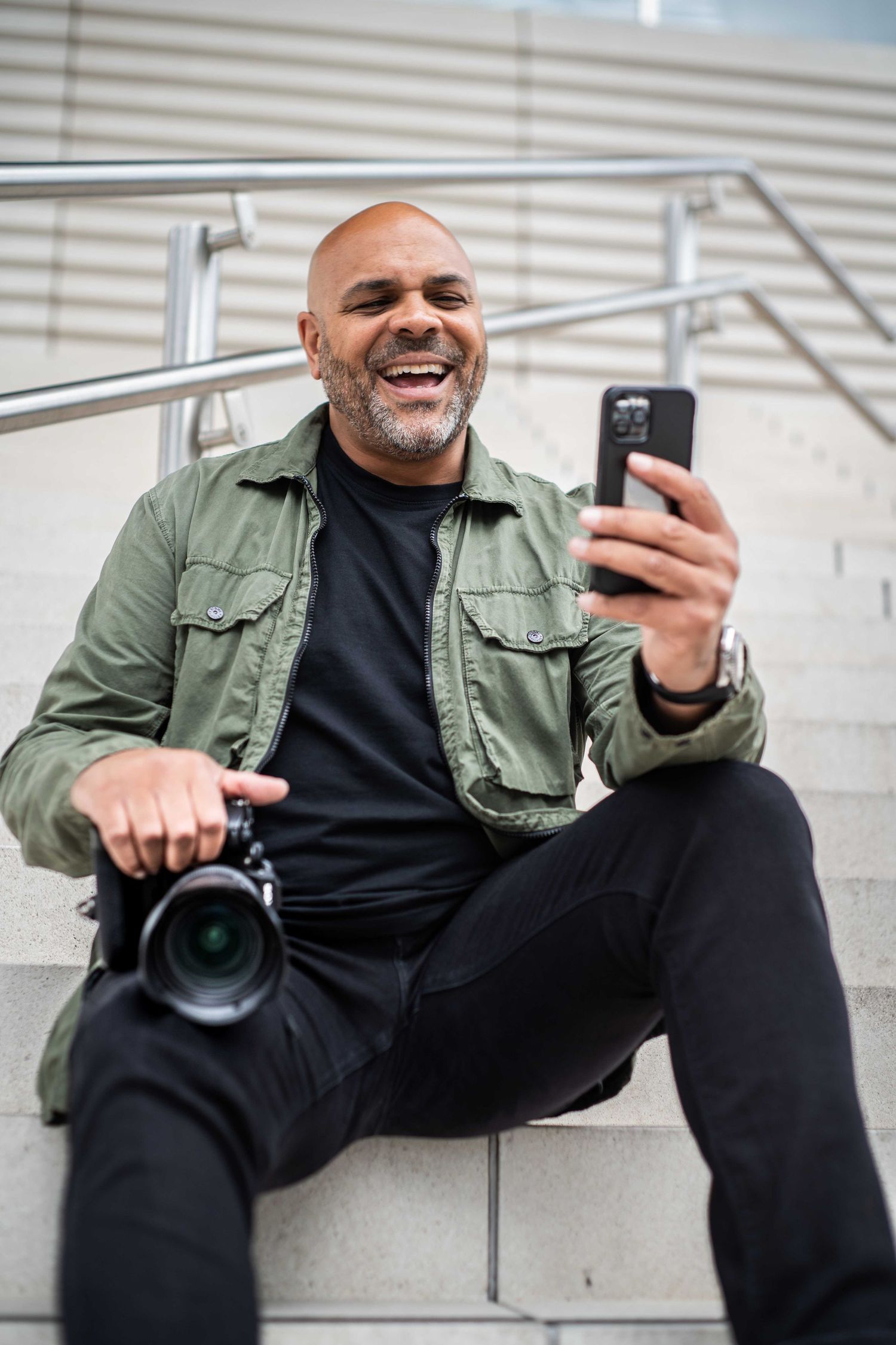 Personal brand photographer Steve Currie sits looking at his phone on the steps at West Quays, Southampton. He's holding a camera