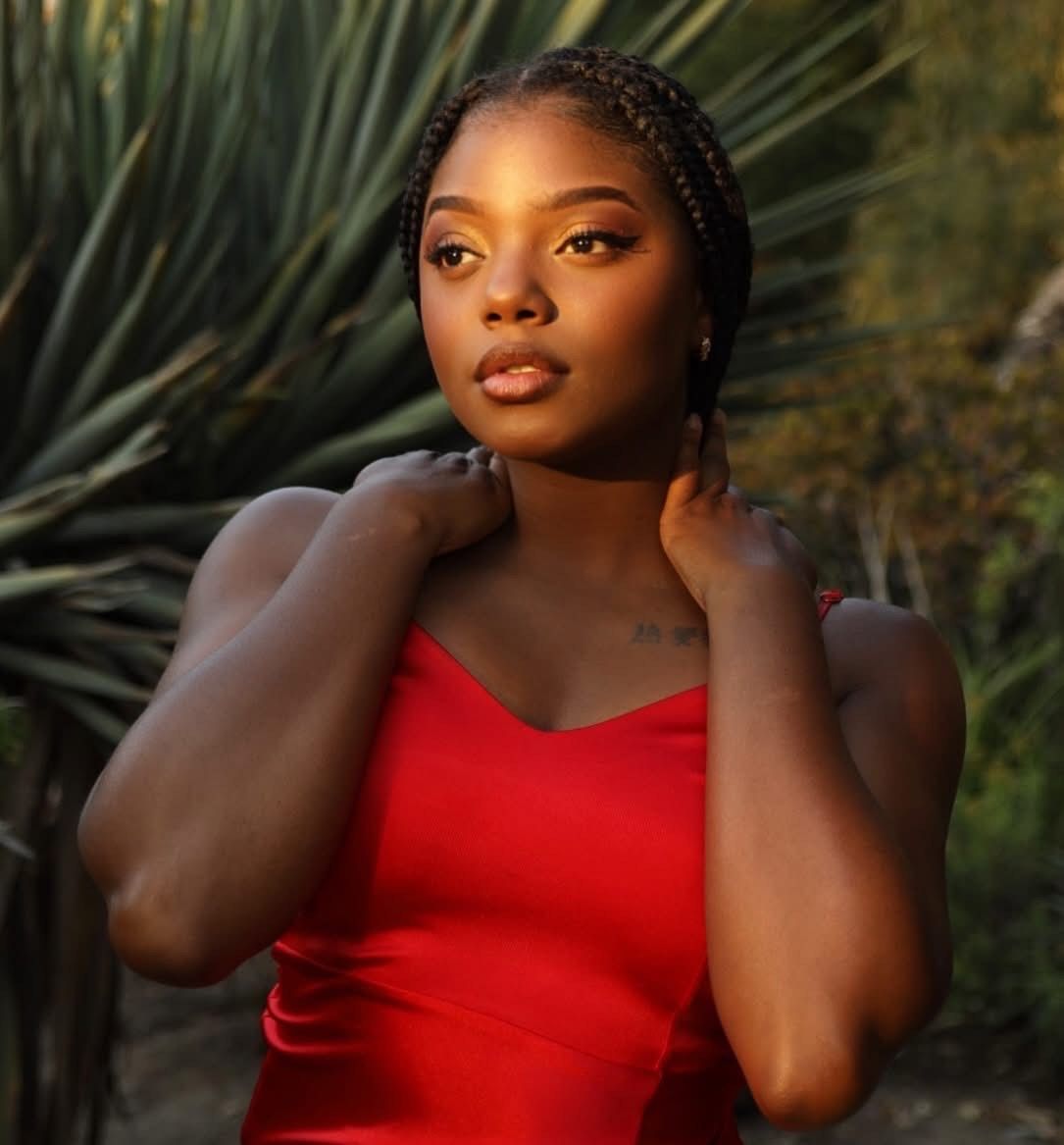 Dreamy natural light portrait of a beautiful Black woman wearing a flowing romantic dress amongst large cacti plants.
