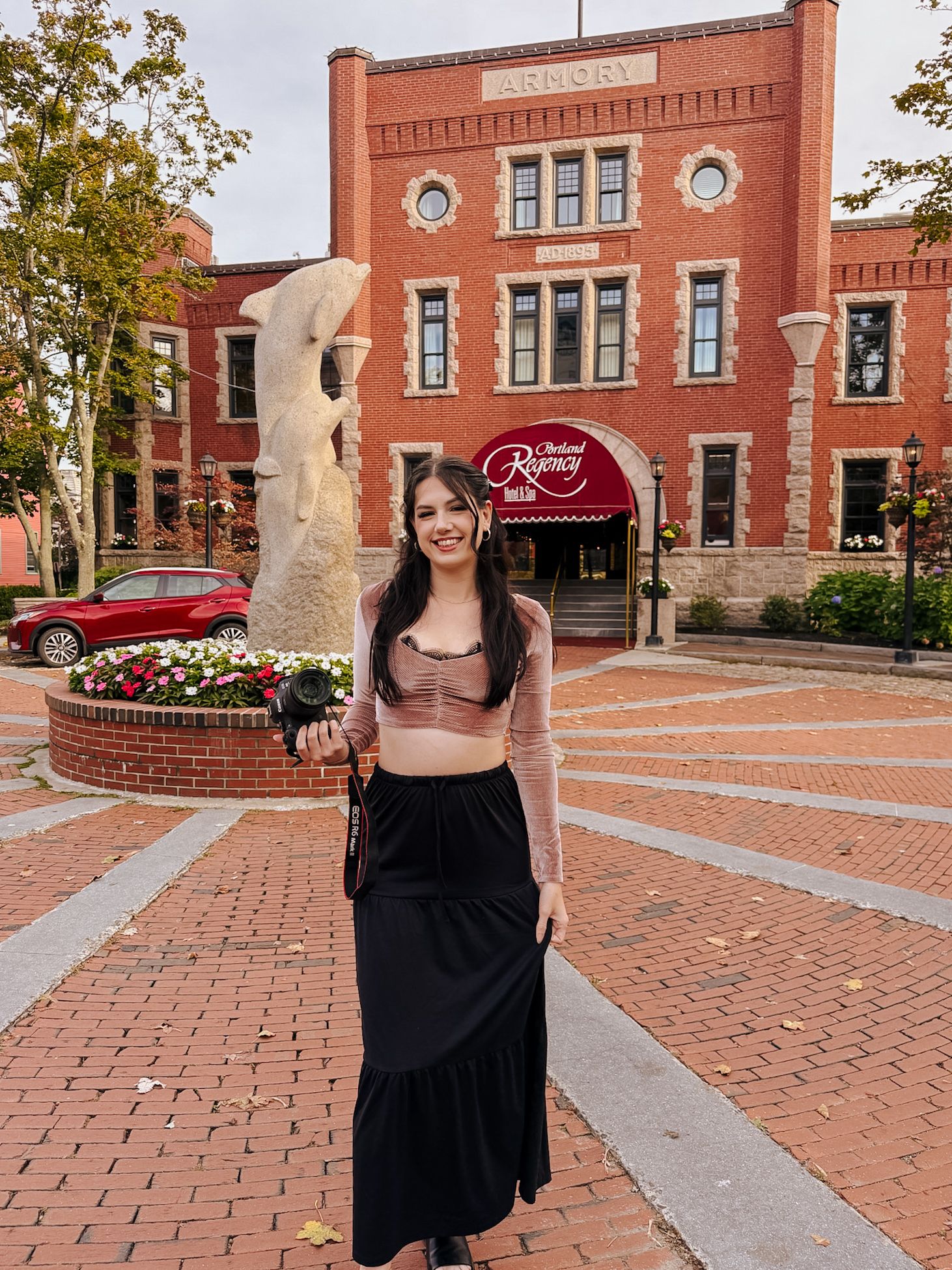 Woman in black maxi skirt poses in front of historic brick Radisson hotel building on decorative brick plaza.