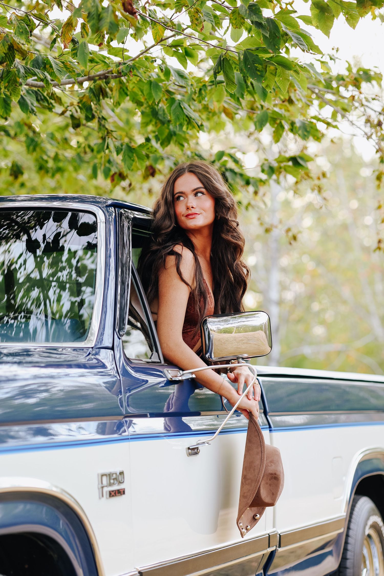 A stylish portrait outdoors against a vintage white and blue truck under green foliage.