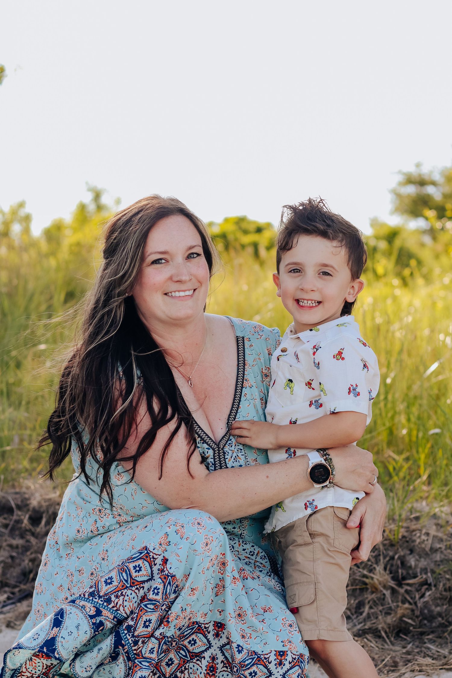An outdoor portrait of a mother and son in a summer field with tall grass and warm lighting.