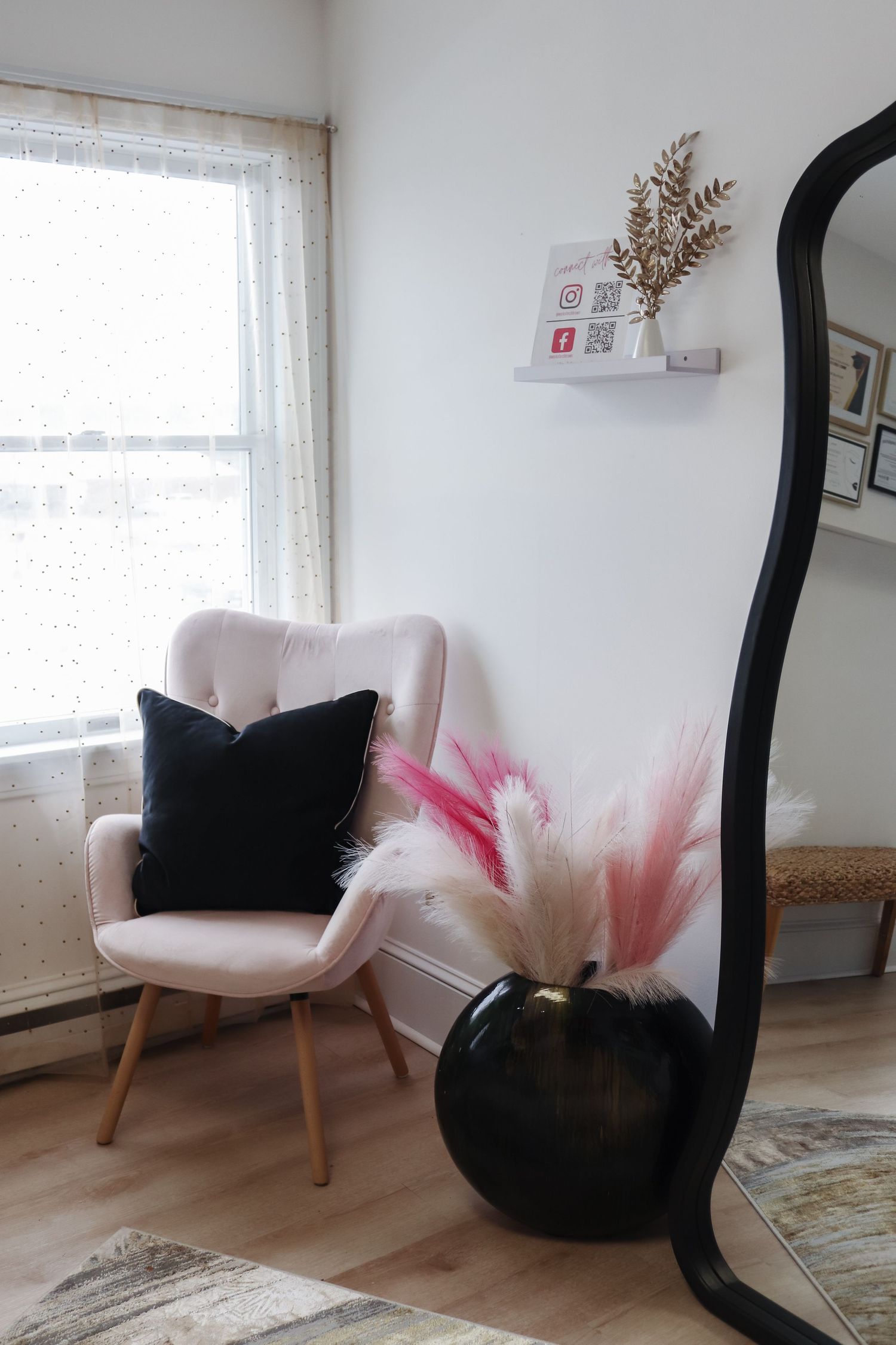 Modern pink accent chair with wooden legs sits in bright corner room with white walls and natural lighting.