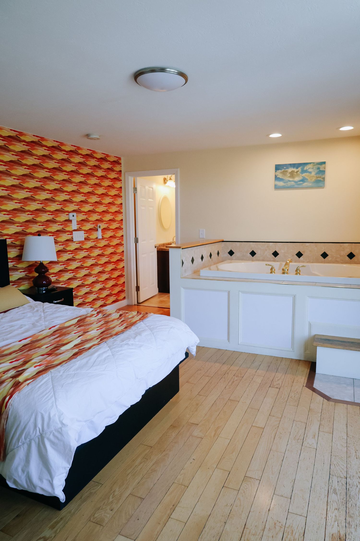 Modern hotel room interior with white bedding and geometric orange wallpaper pattern photographed for hotel marketing in Maine