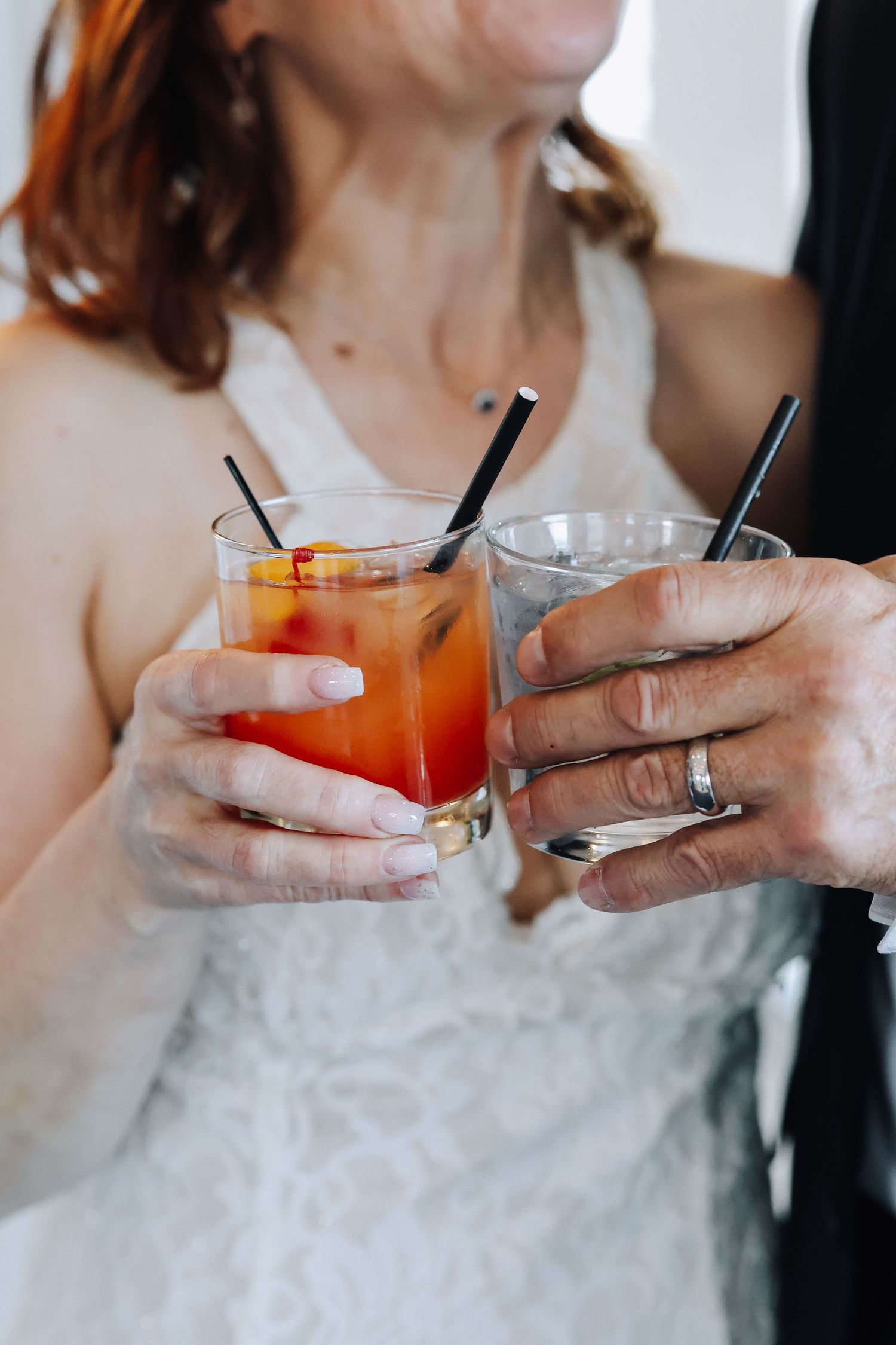Two hands holding colorful cocktails in glasses clink together in a celebratory toast.