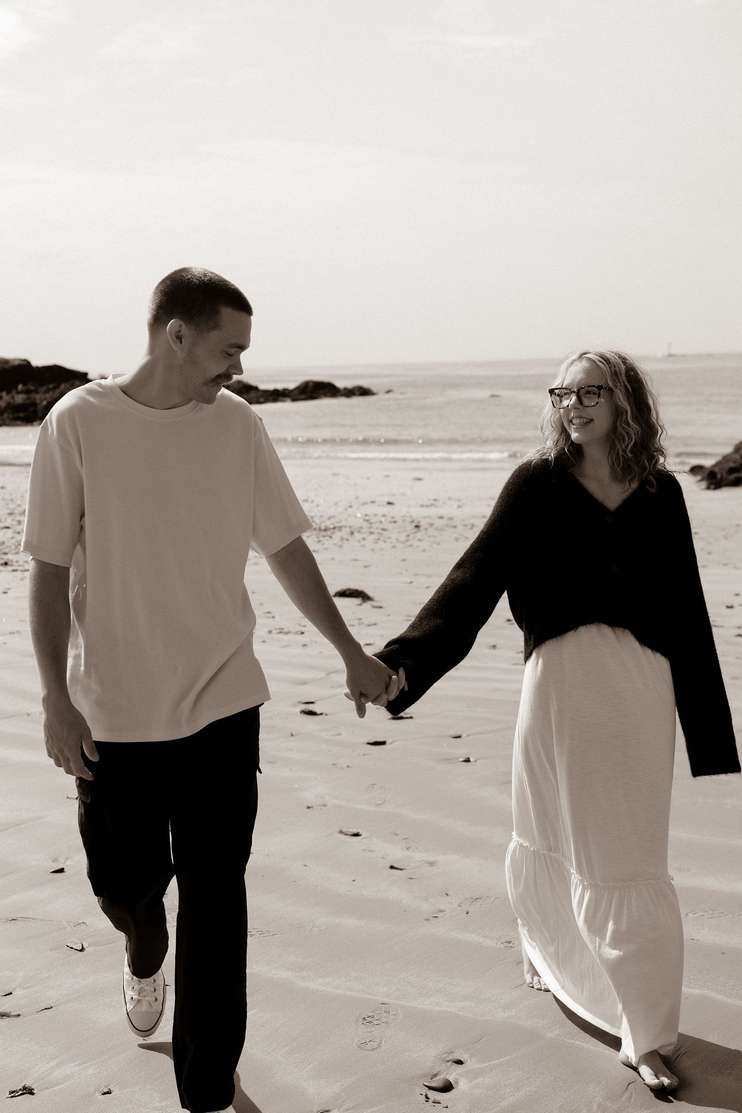 Black & white image of couple walking on the beach, holding hands