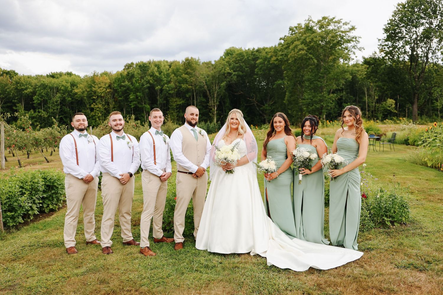 Wedding party poses in a garden wearing sage green dresses and khaki suits on a summer day.