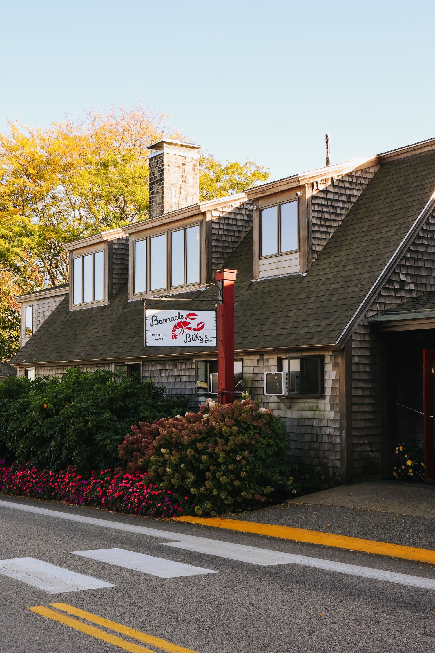 Barnacle Billy's seafood restaurant exterior with cedar shingle siding, large windows, and colorful landscaping on a quiet street.