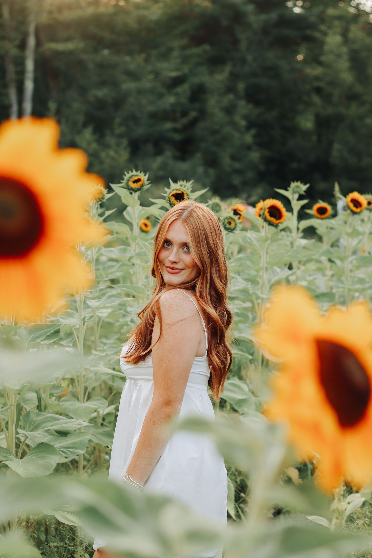 A solo female summer photoshoot in a vibrant sunflower field with soft natural lighting.