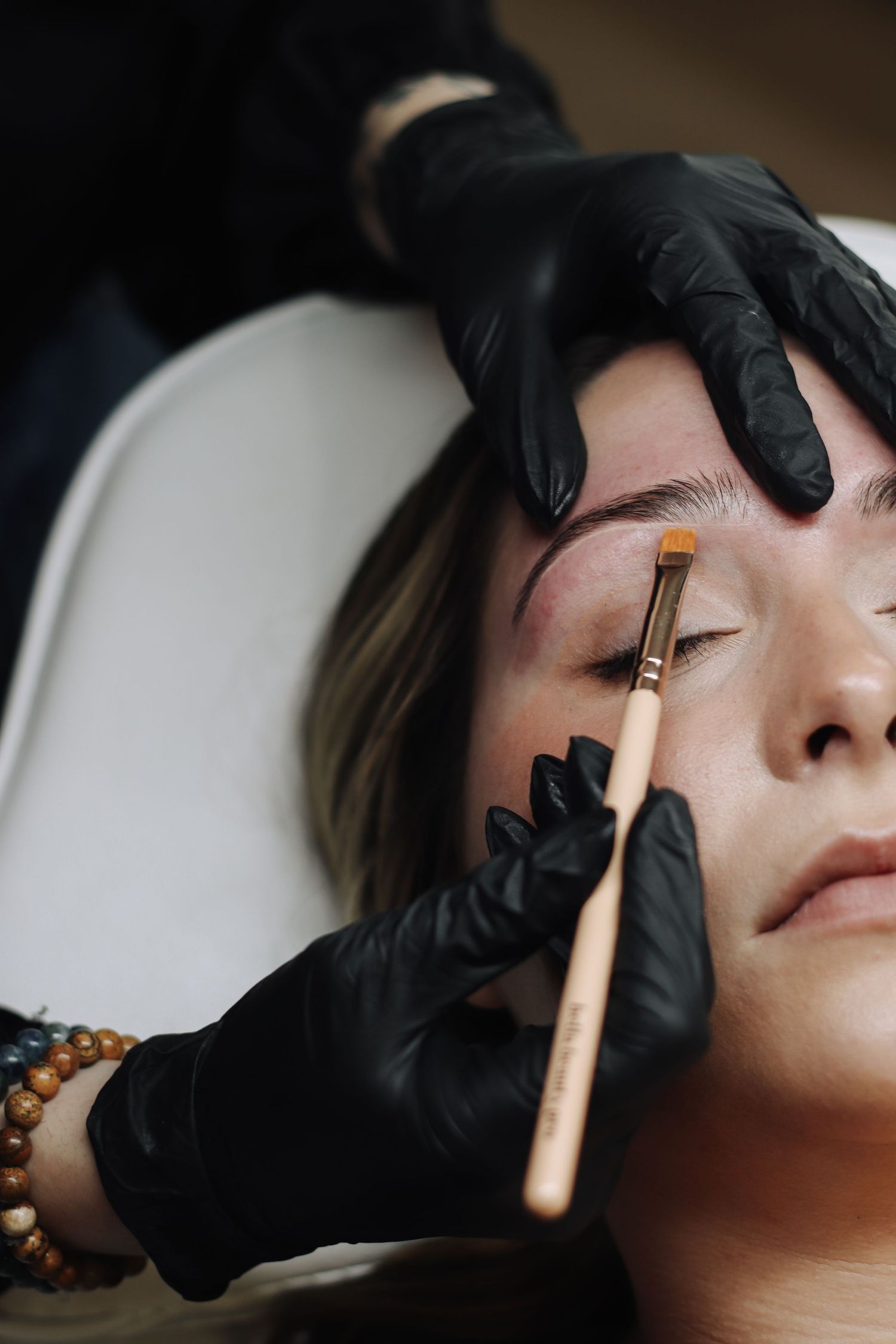 A close-up sequence showing an eyebrow tinting or microblading beauty treatment being performed with a small brush.