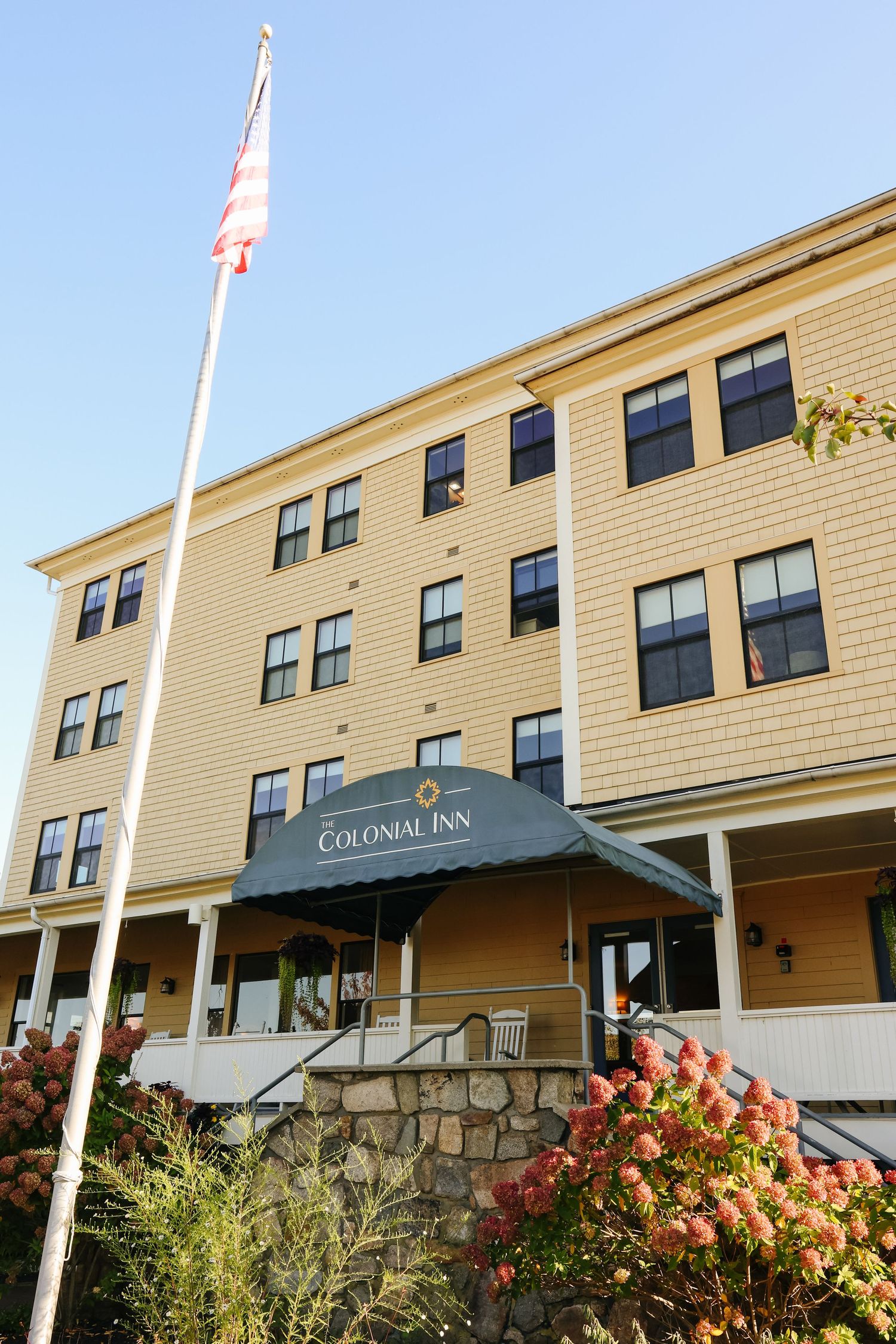 Exterior view of a beige Colonial Inn building with multiple windows and a flagpole against blue sky.