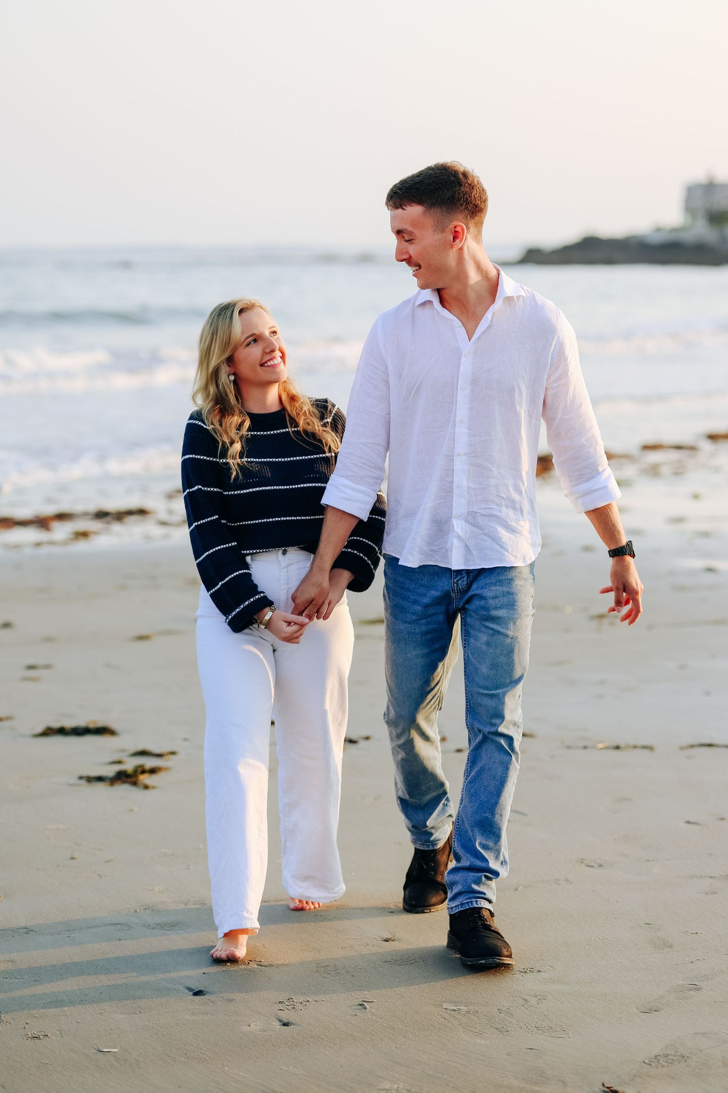 A couple takes a romantic stroll along the beach at sunset.