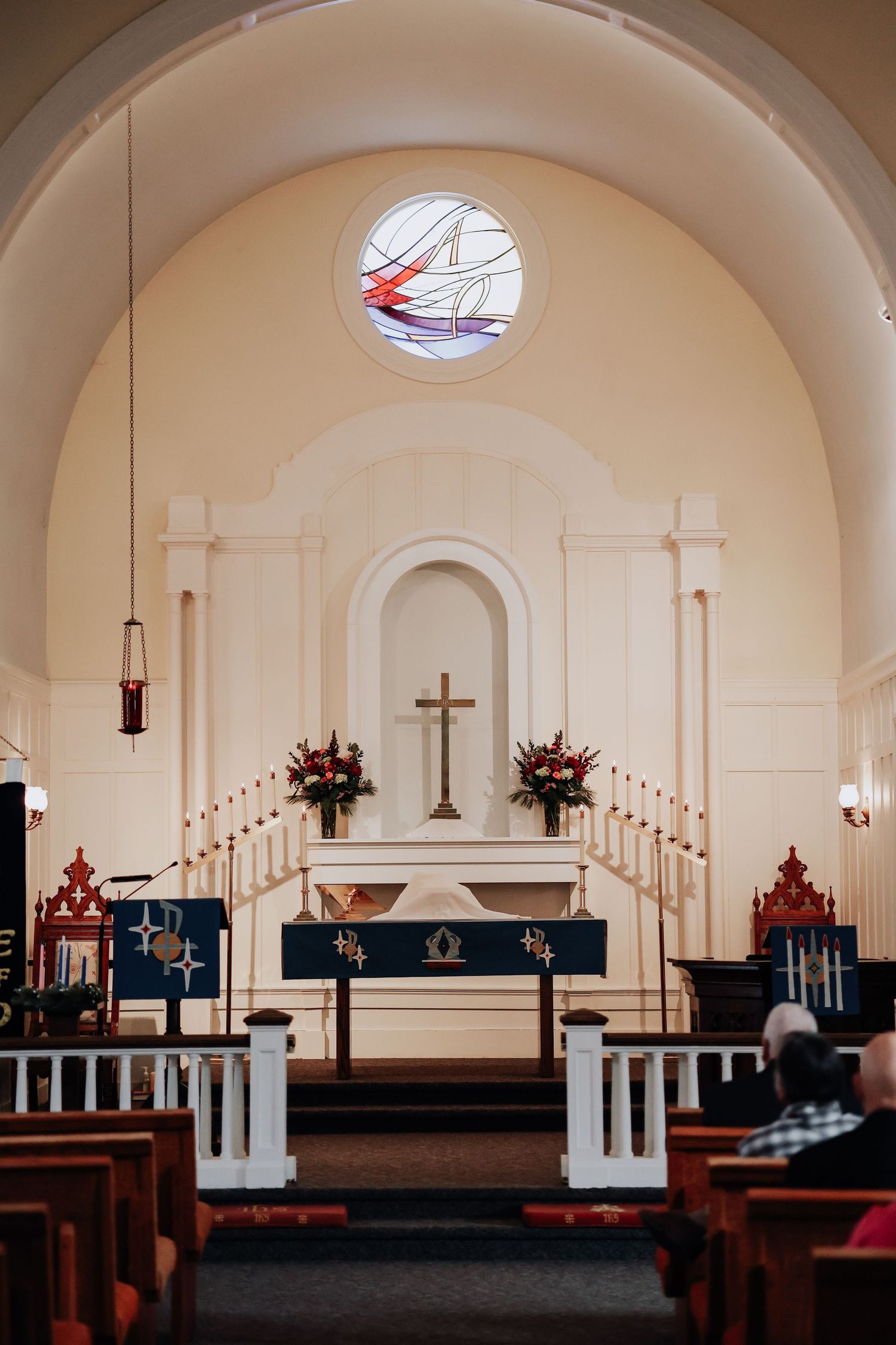 Interior view of a traditional church sanctuary with white arched walls, wooden pews, and a simple altar with candles.