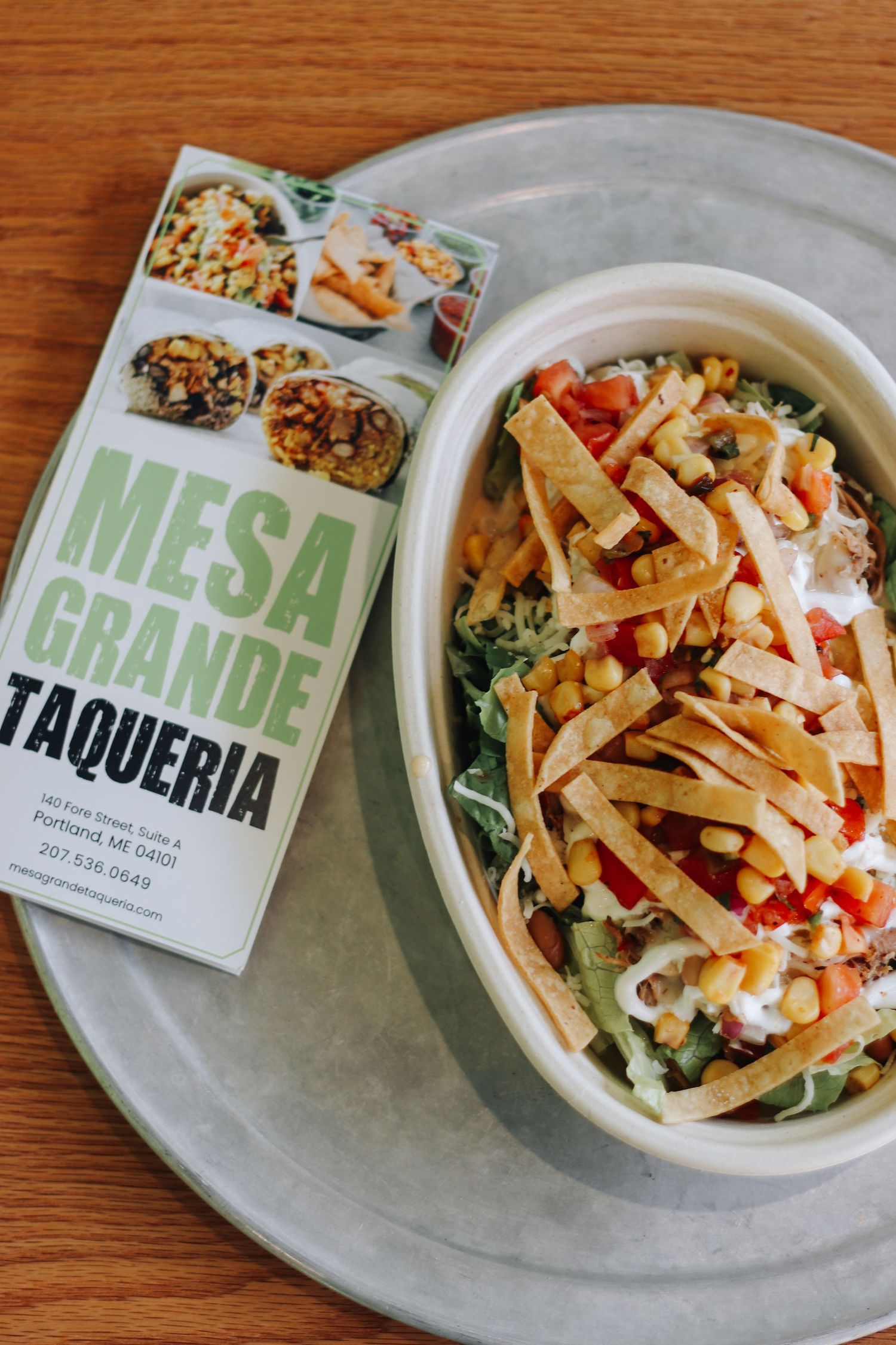 Mesa Grande Taqueria menu card beside a fresh taco salad with tortilla strips, corn, and veggies in a bowl.