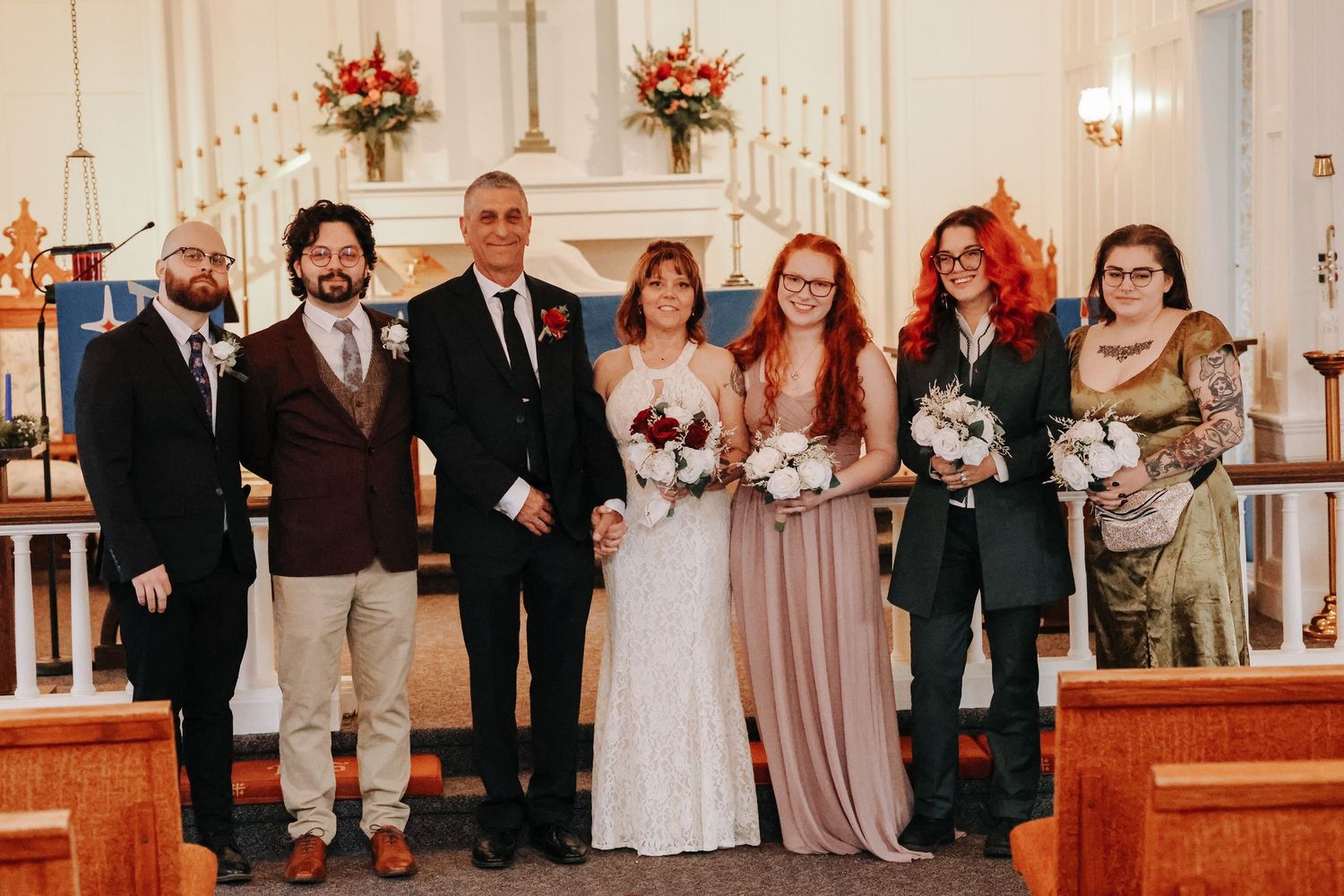 A wedding party poses together in a church with floral decorations and candelabras in the background.