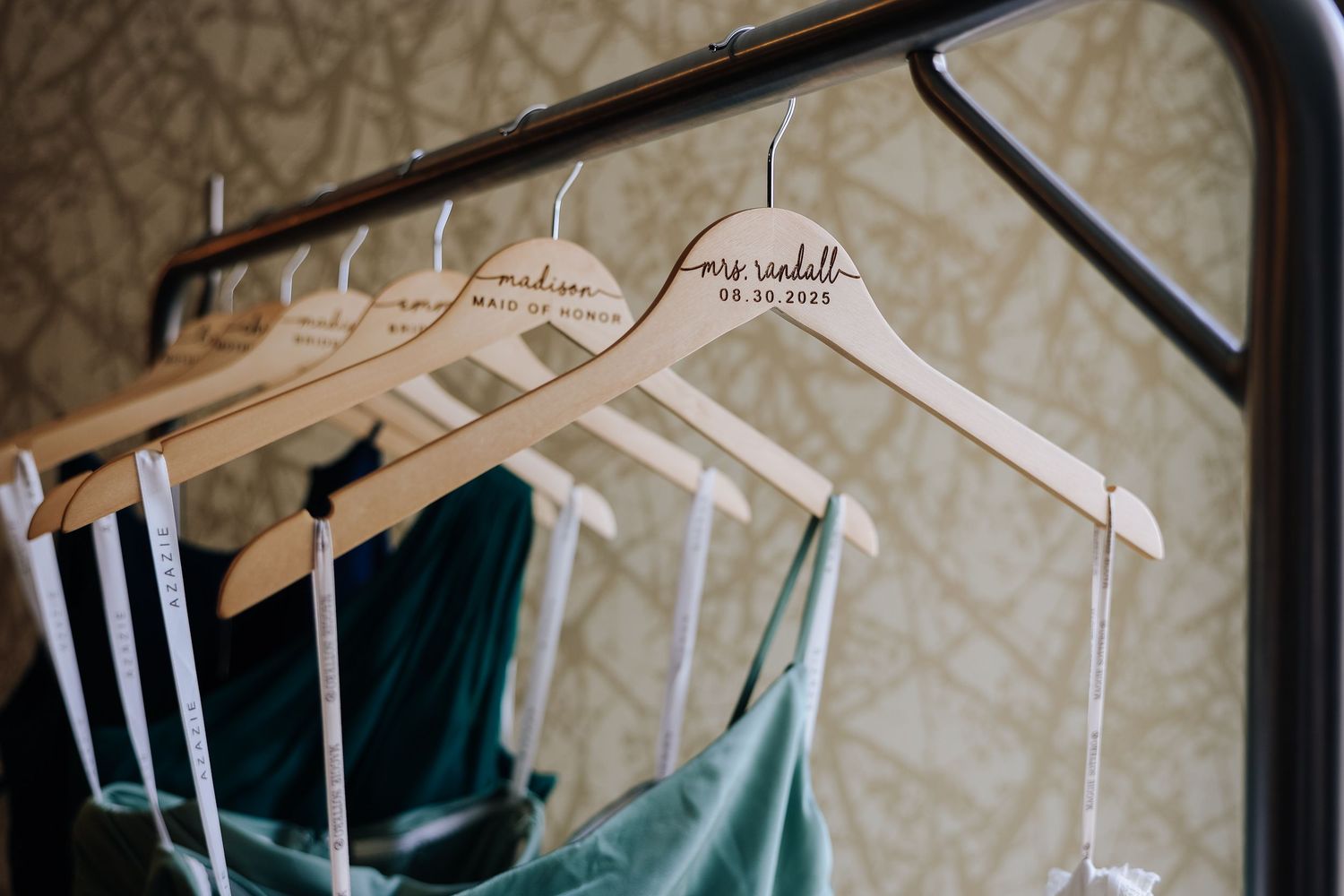 Wedding day details- wooden hangers displayed on a clothing rack against patterned wallpaper.