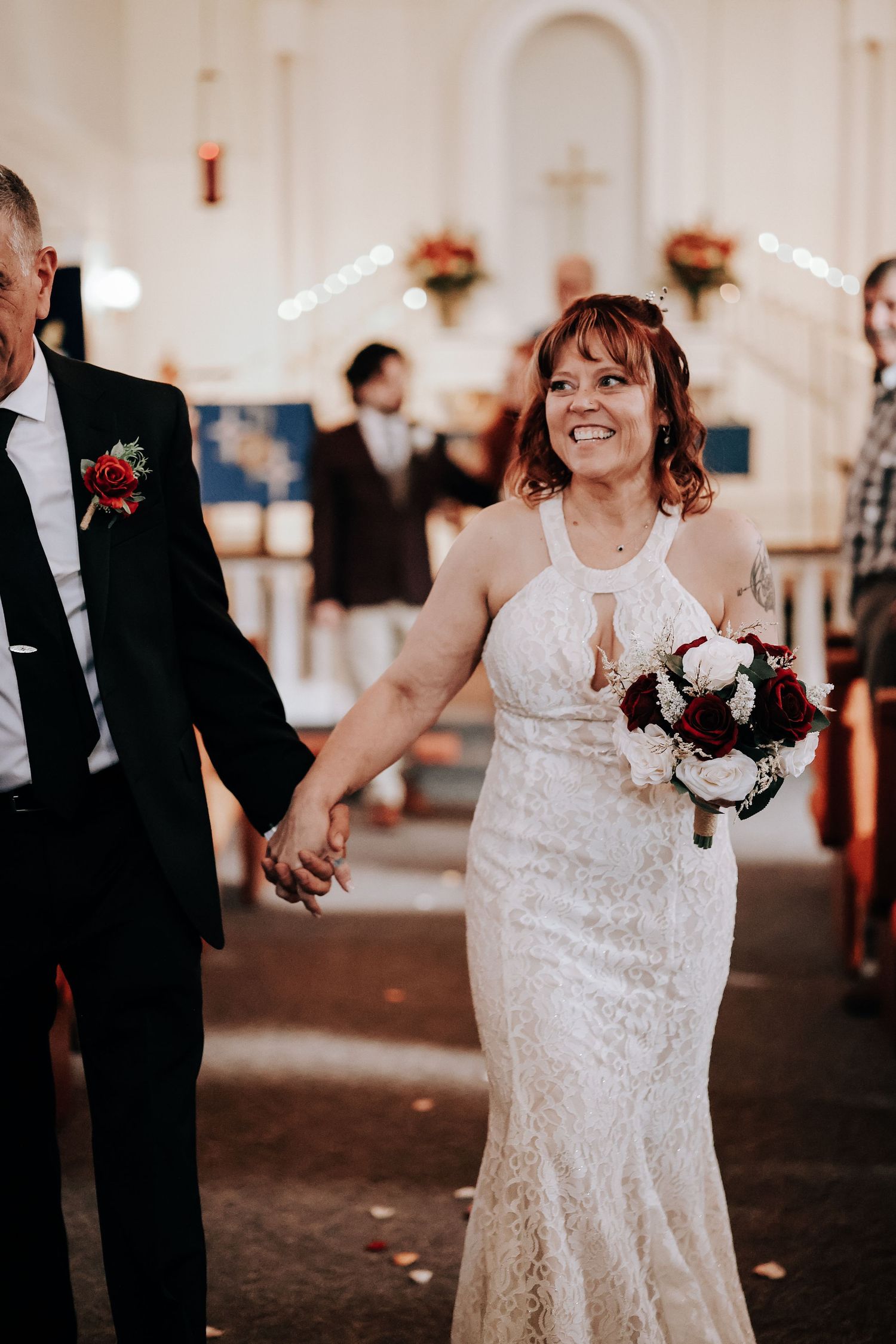 A bride in a white lace dress walks down a church aisle during a wedding ceremony.