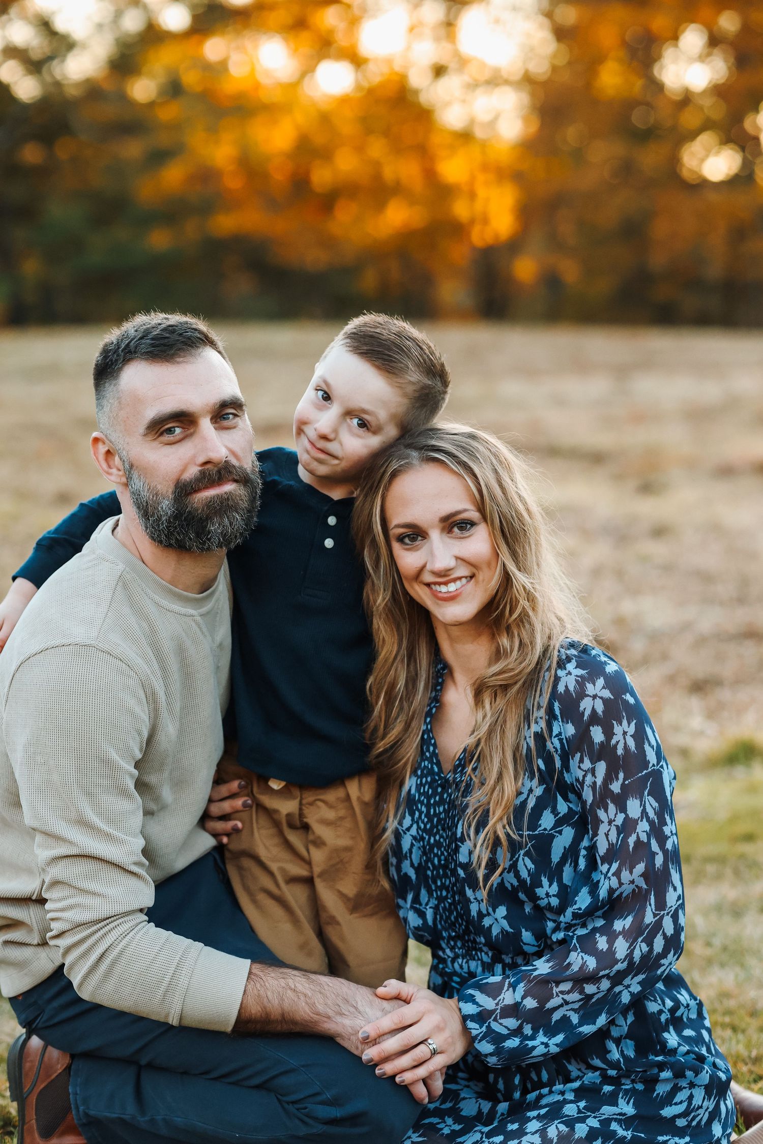 A happy family poses together outdoors during golden hour in autumn.