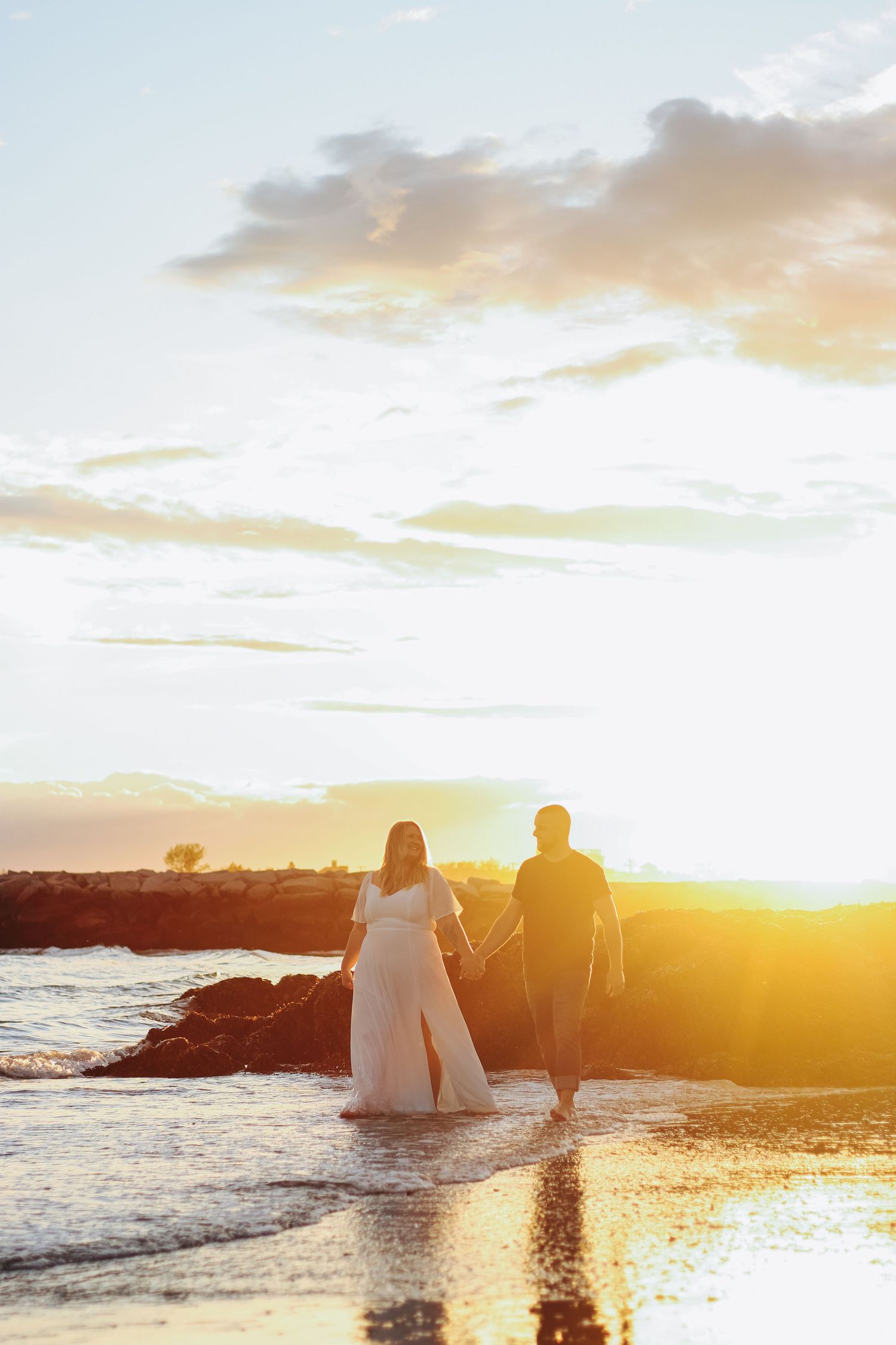 Silhouette of couple walking along rocky coastline during dramatic golden sunset.