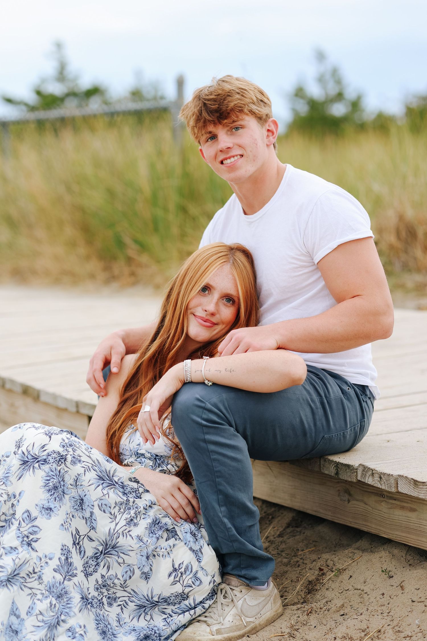 A couple poses intimately on a wooden boardwalk at the beach.