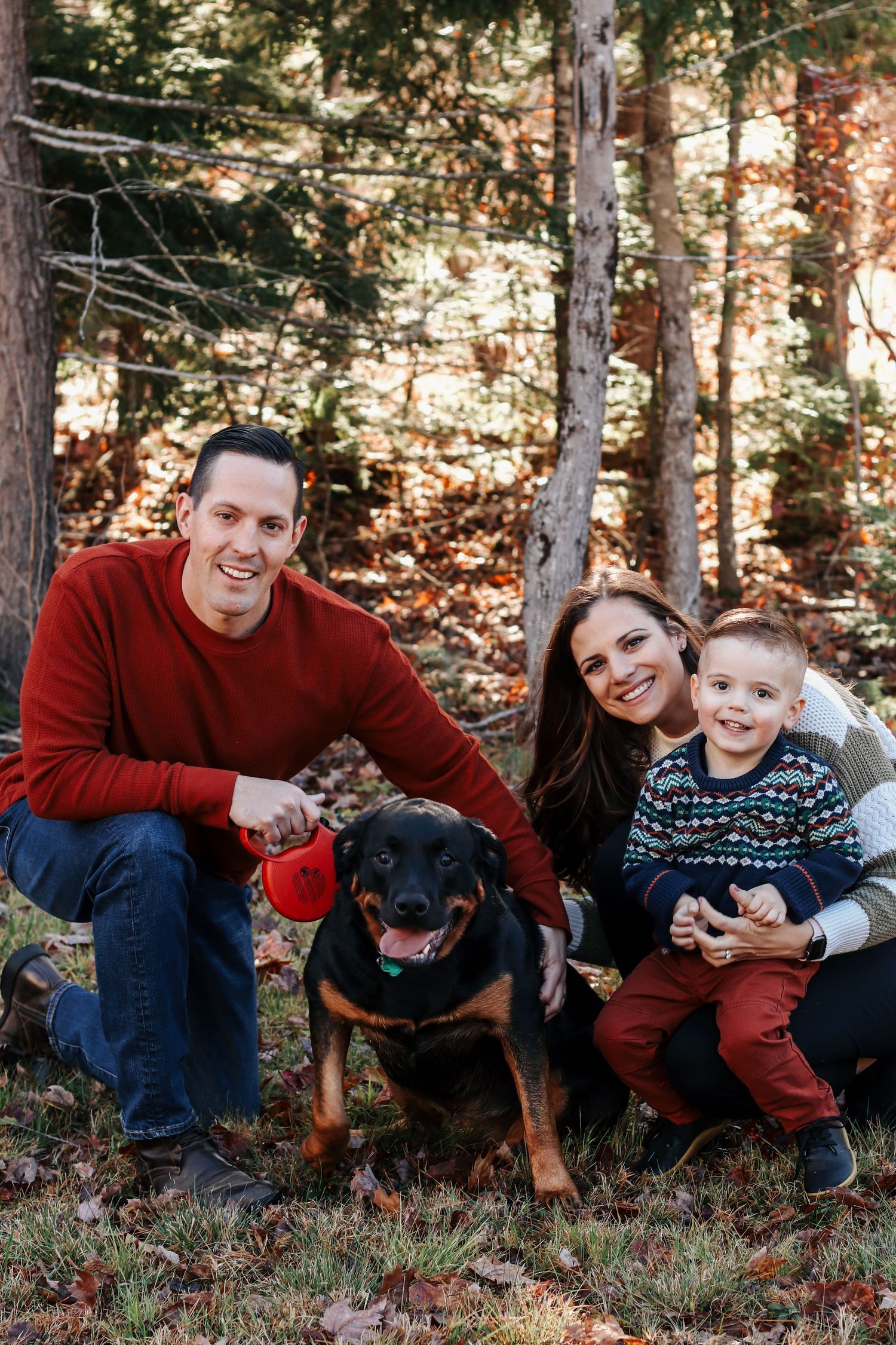 A family and their black dog pose together for outdoor portraits in a wooded setting.