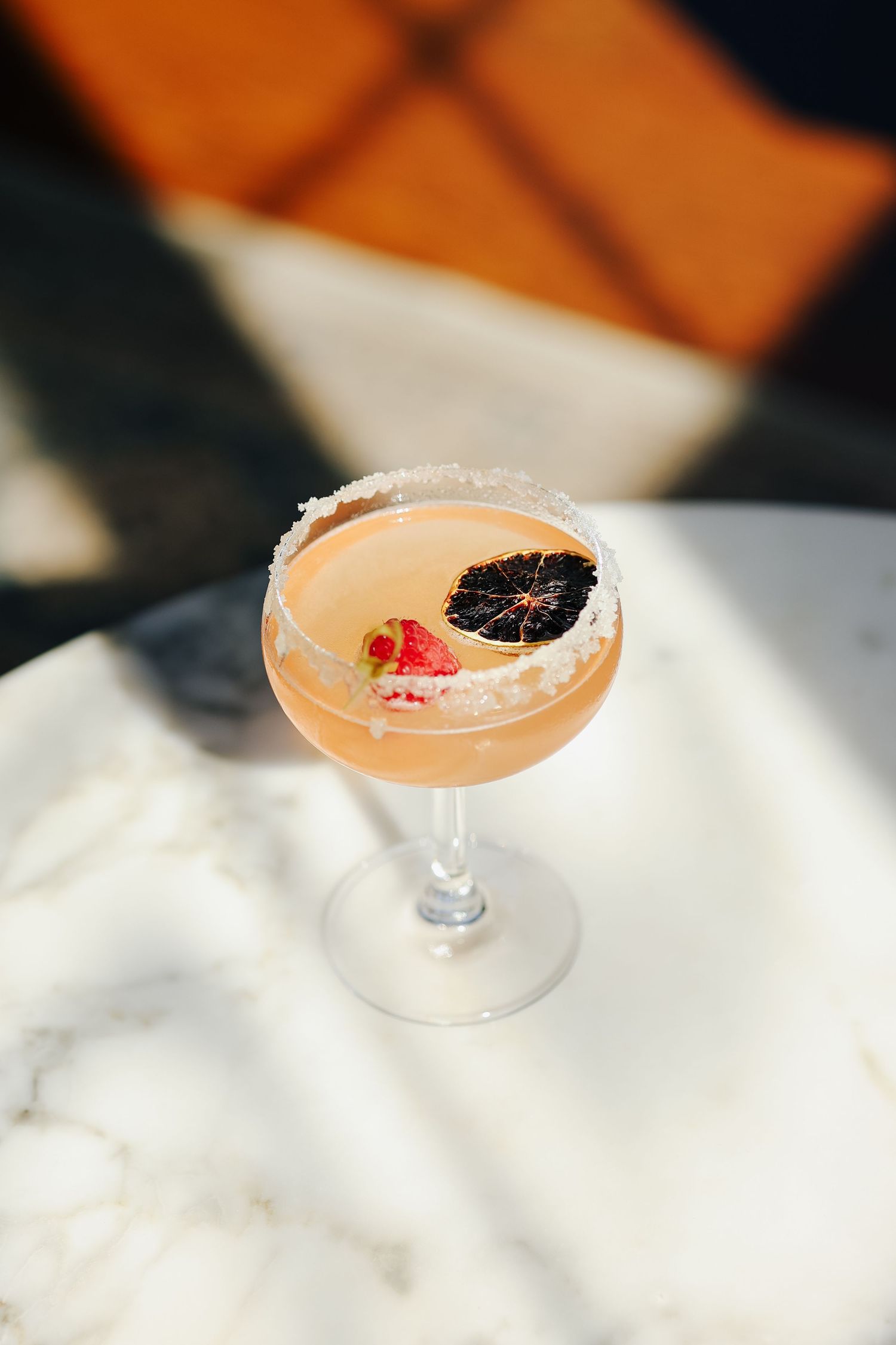 Elegant cocktail in a sugar-rimmed coupe glass garnished with dried blood orange and strawberry on marble surface.