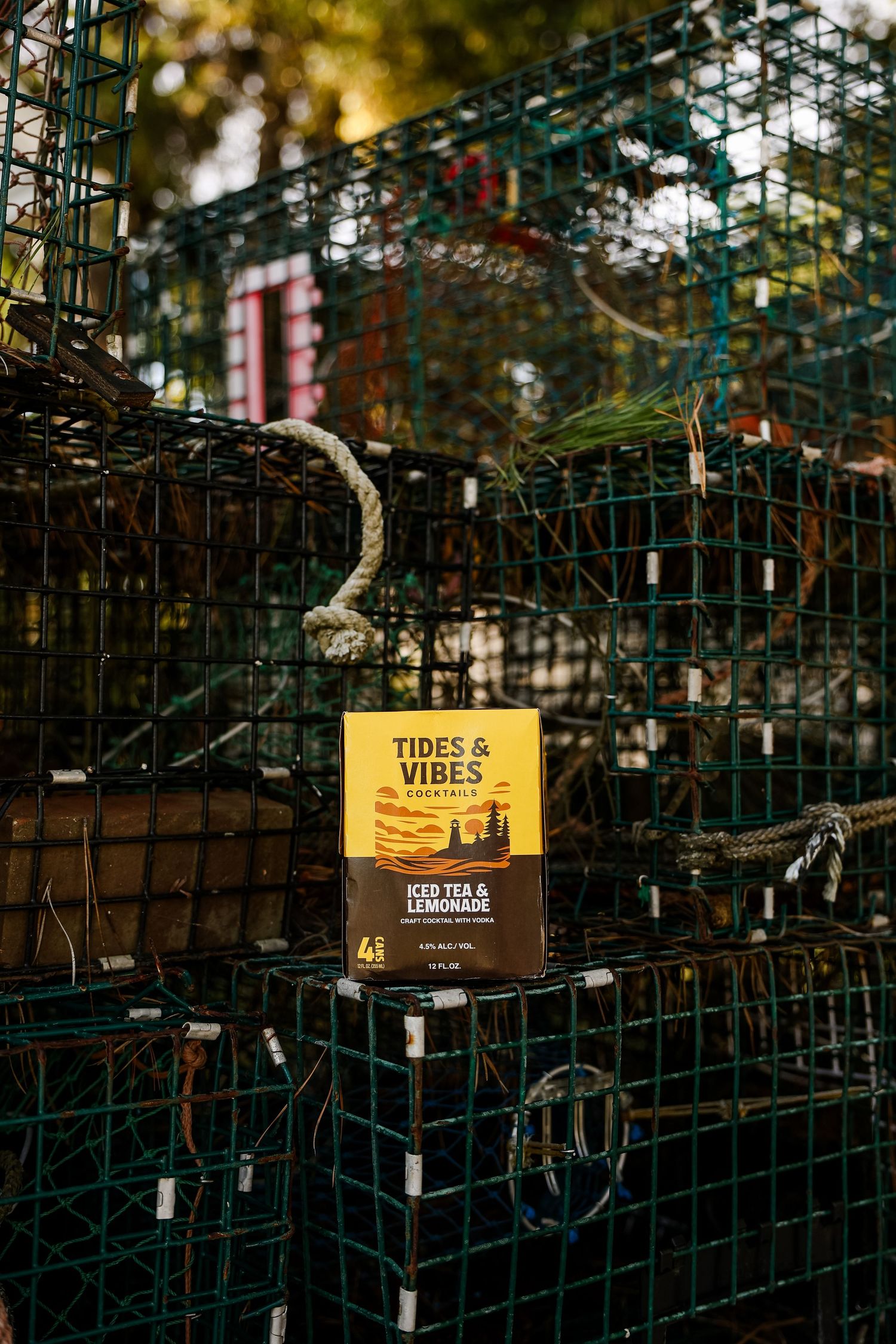 Tides & Vibes iced tea and lemonade cocktail box displayed on stacked green wire lobster traps with rope in warm coastal light.