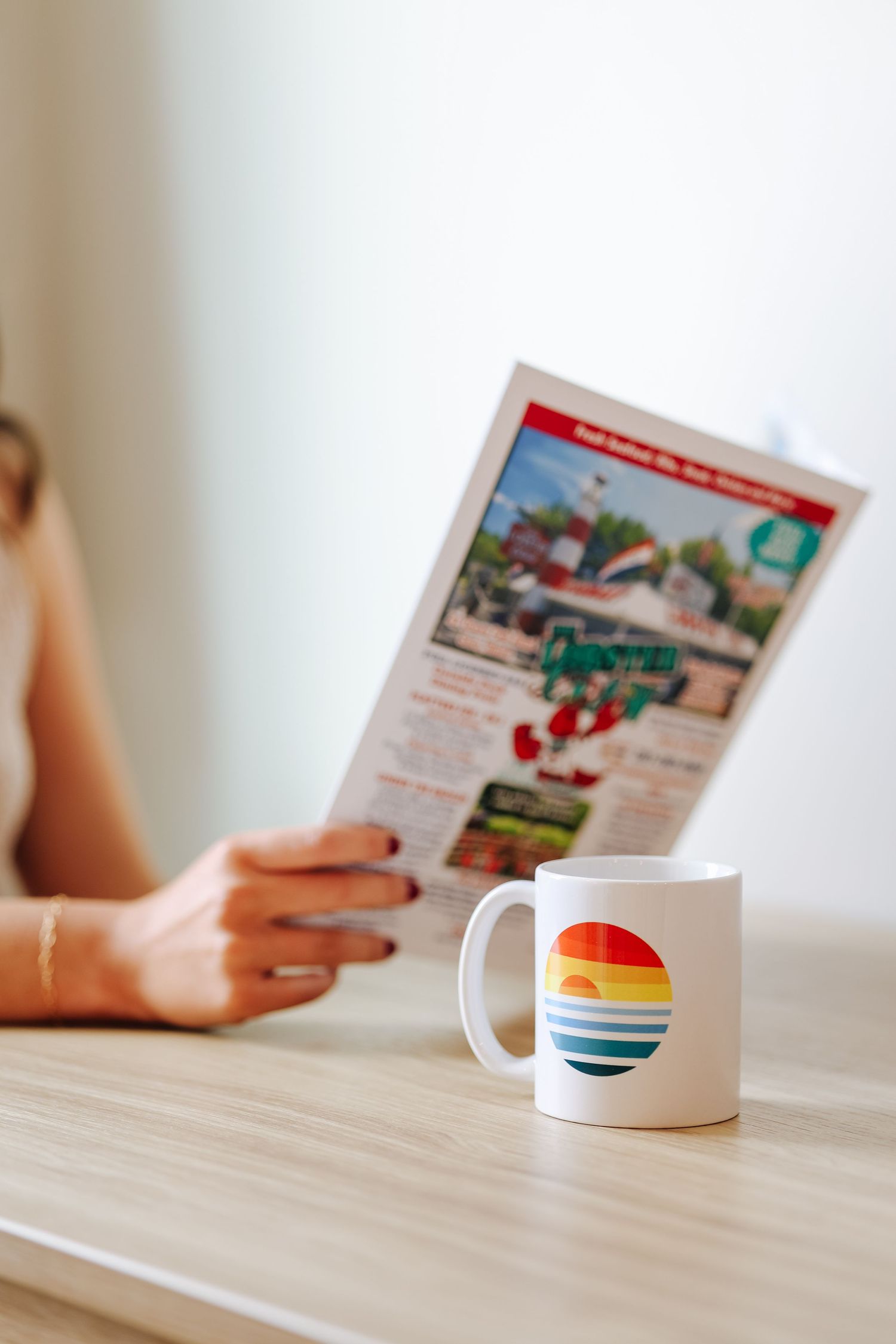 Coffee mugs with sunset designs sit on wooden table next to reading material for hotel marketing in Maine