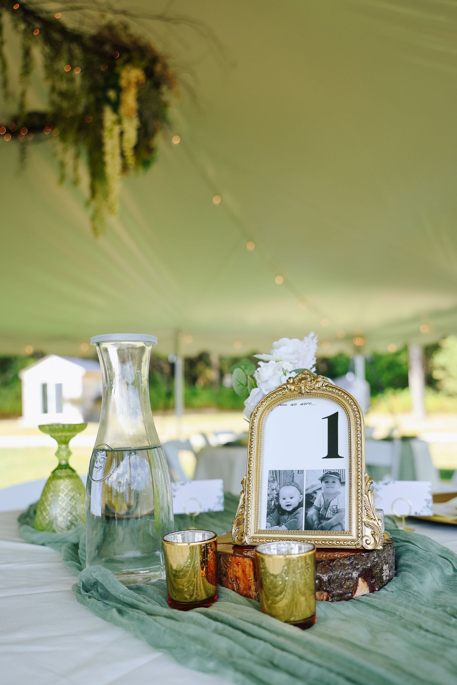 Vintage-inspired table decor with gold frames and green accents under tent lighting.