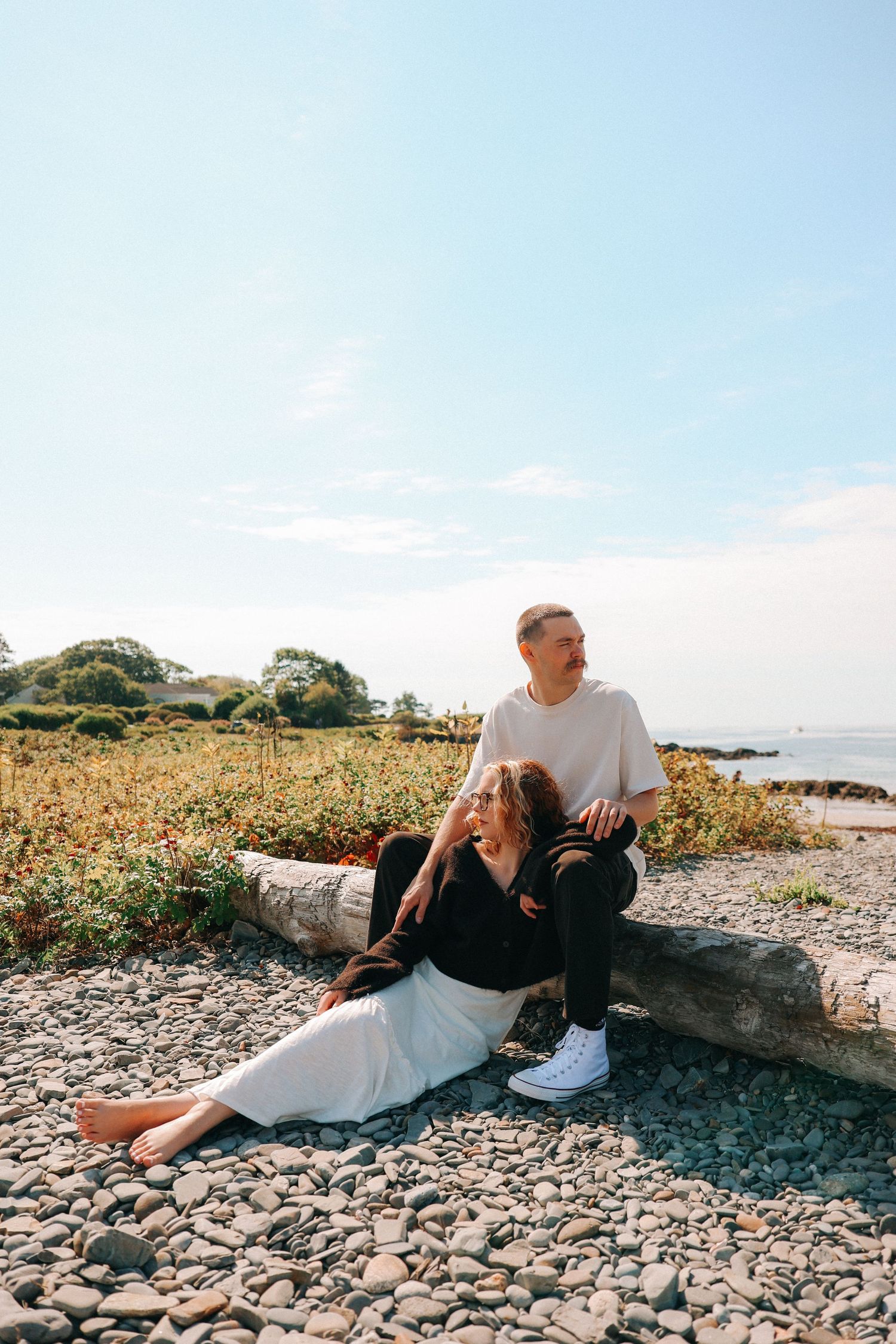 A couple relaxes together on rocky coastal terrain with ocean views.