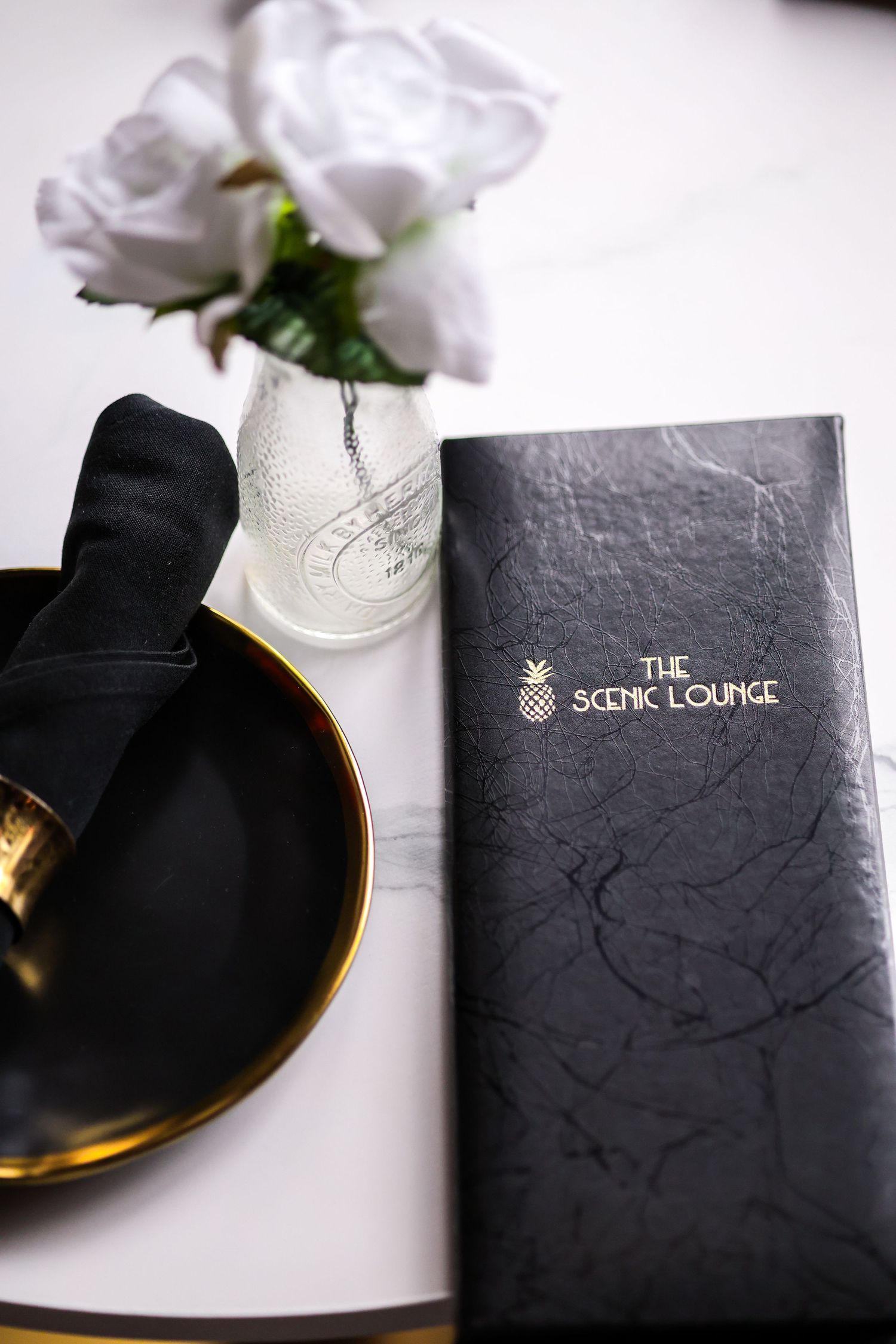 Elegant table setting with white roses, a black menu for The Scenic Lounge, and gold accents.