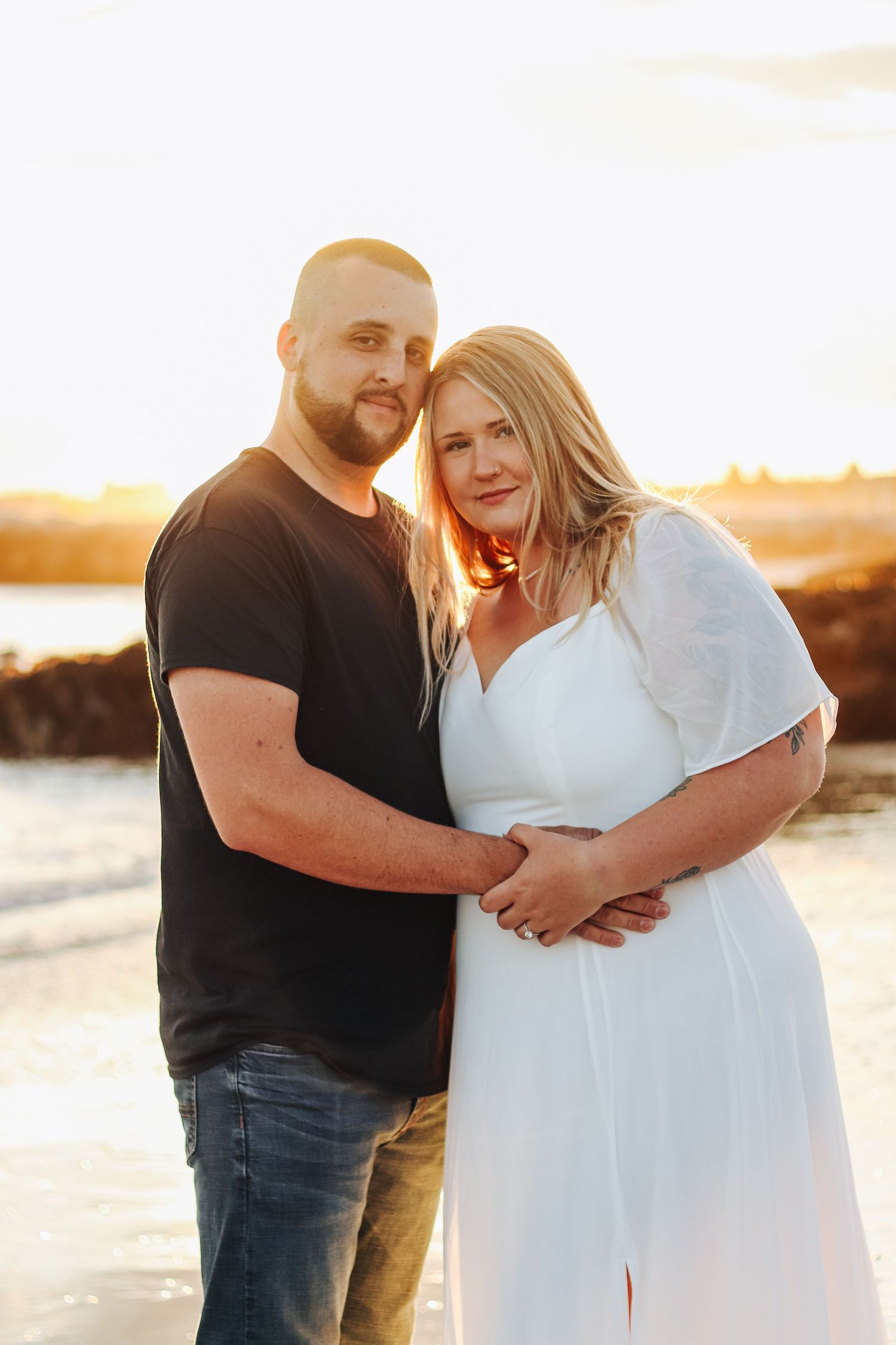 A couple embraces on the beach during a golden sunset photoshoot.