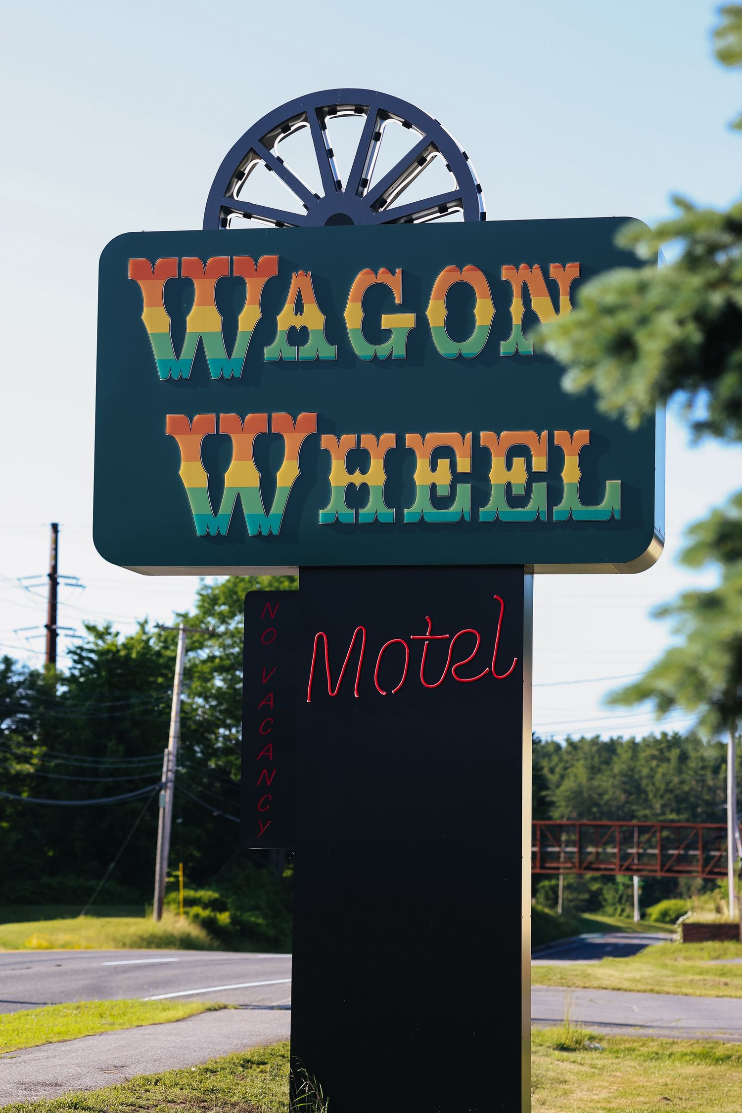 Vintage motel sign for Maine hotel with rainbow colored lettering and wagon wheel design on top.