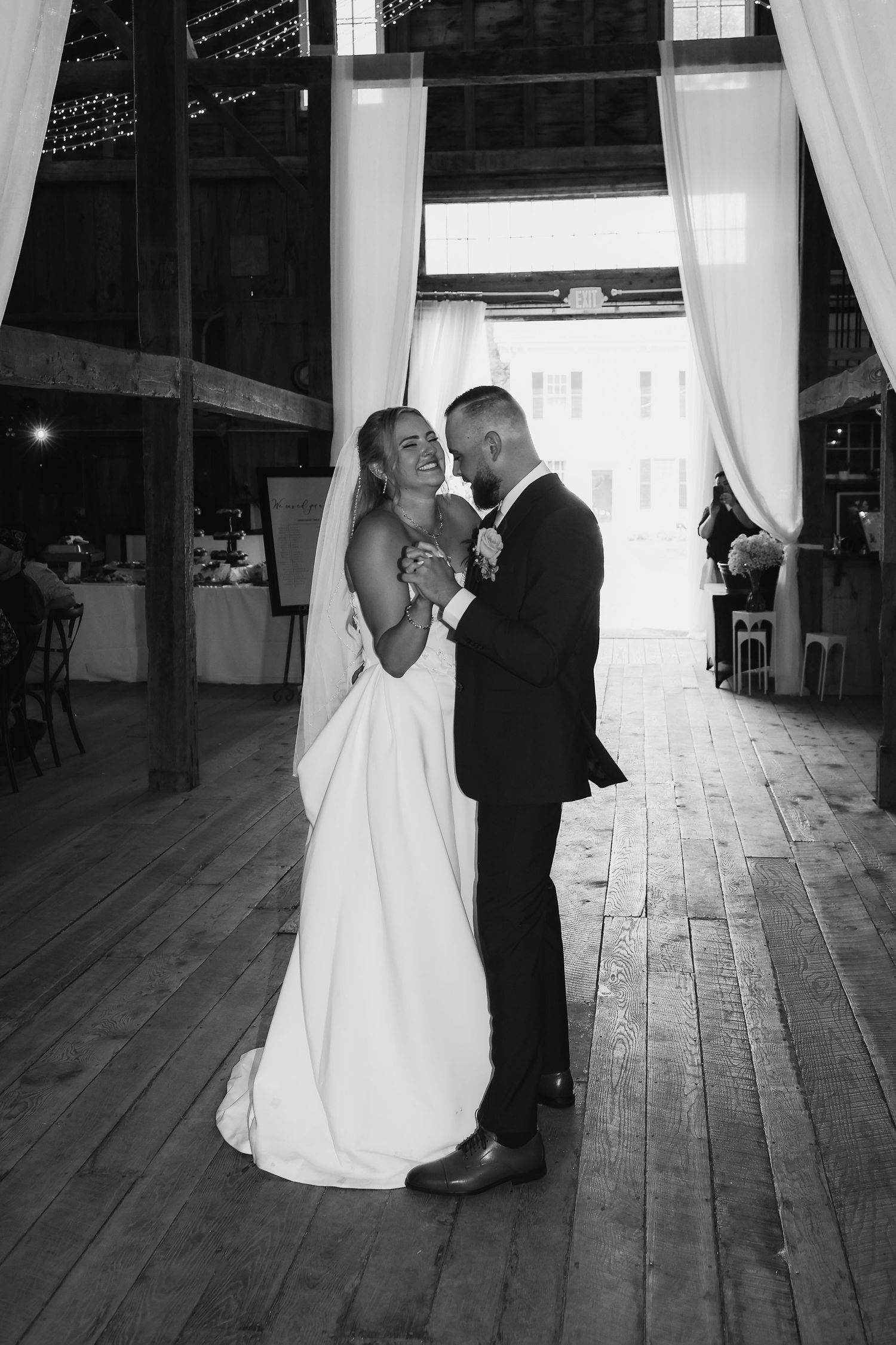 Black and white photo of bride and groom sharing first dance in rustic barn venue.