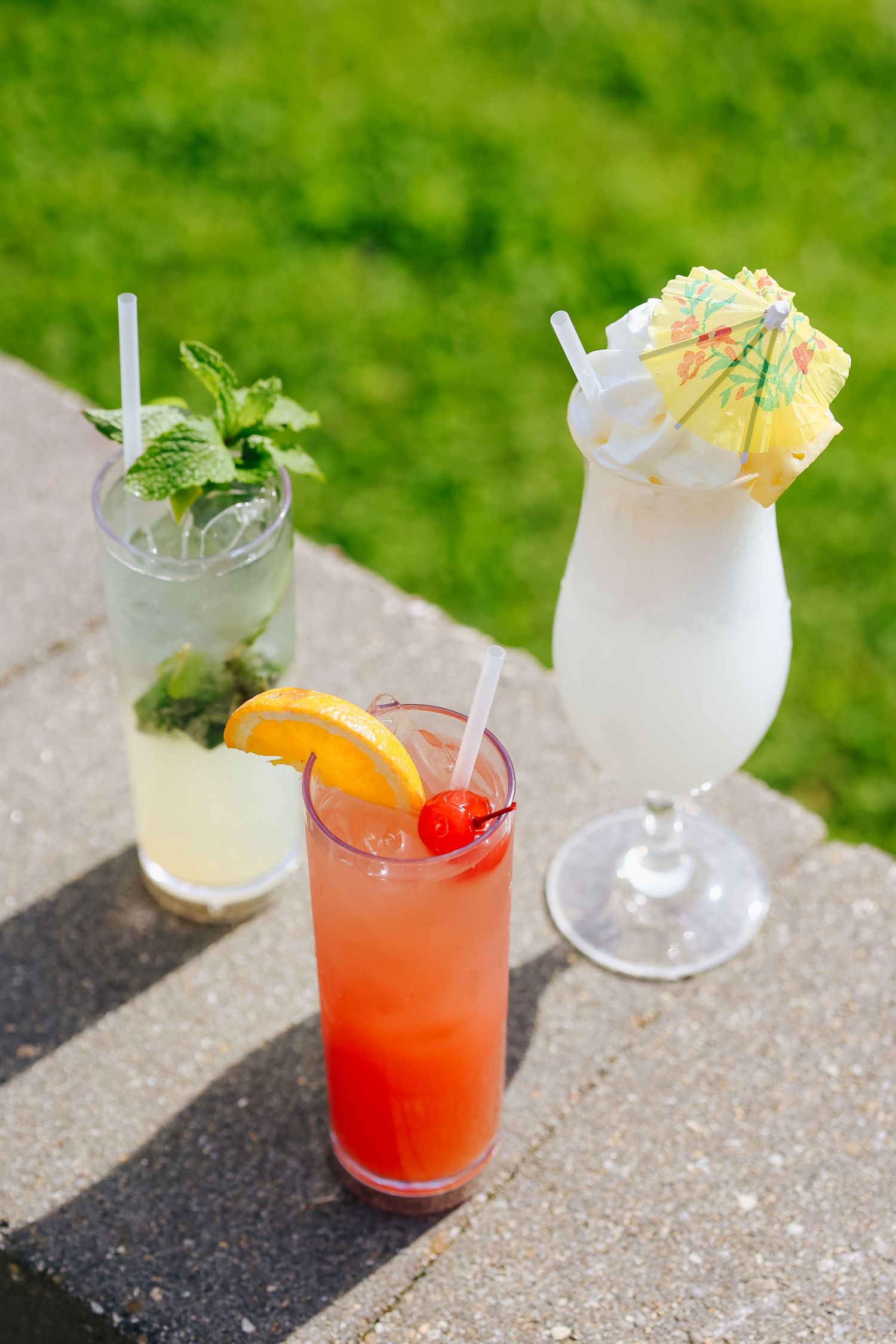 Row of garnished cocktails with citrus and tropical fruits on stone surface outdoors photographed for Ogunquit restaurant marketing