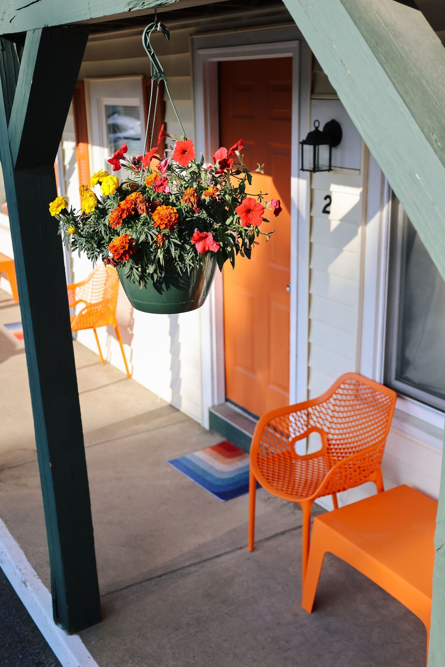 Colorful hanging flower basket and orange patio chair outside a motel room entrance.