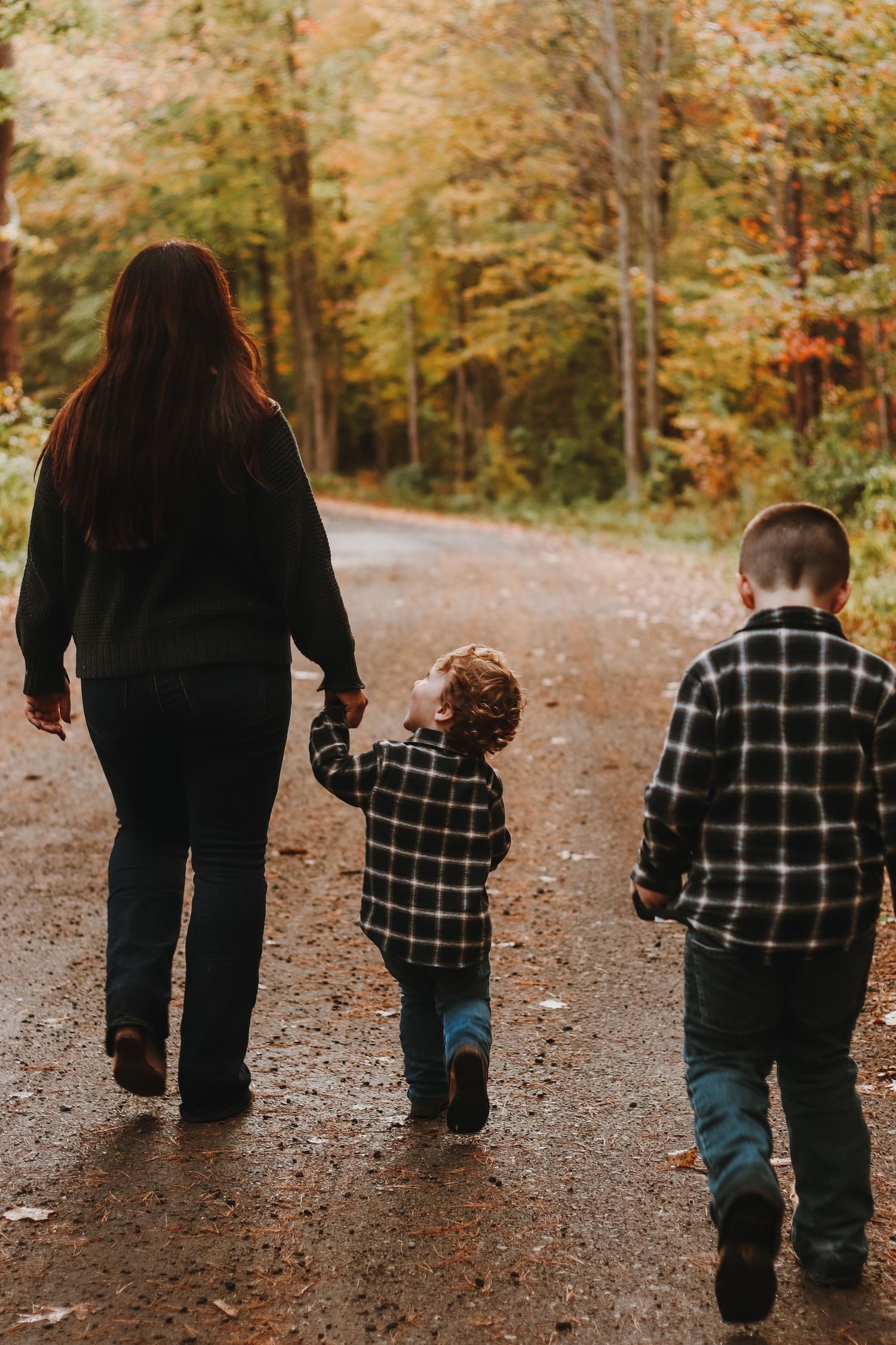 A family takes an autumn stroll together down a leaf-covered path in the woods.