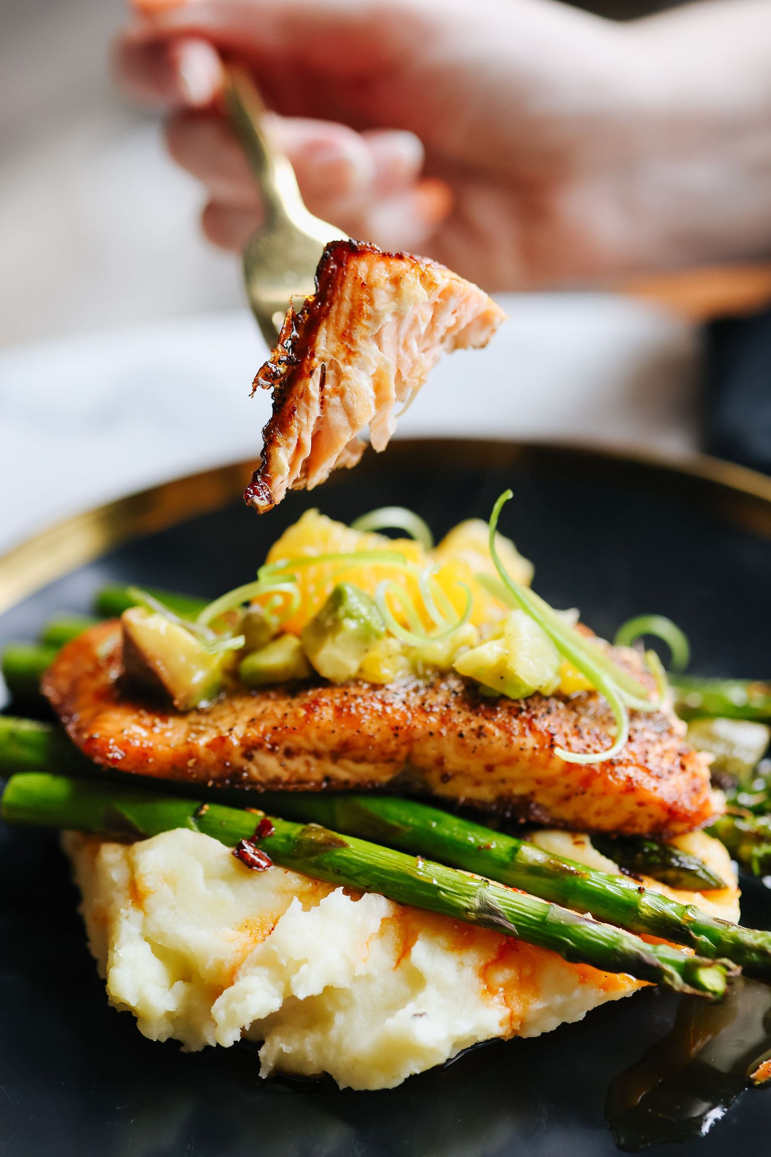 Perfectly plated salmon dish with asparagus and mashed potatoes on black dinnerware.