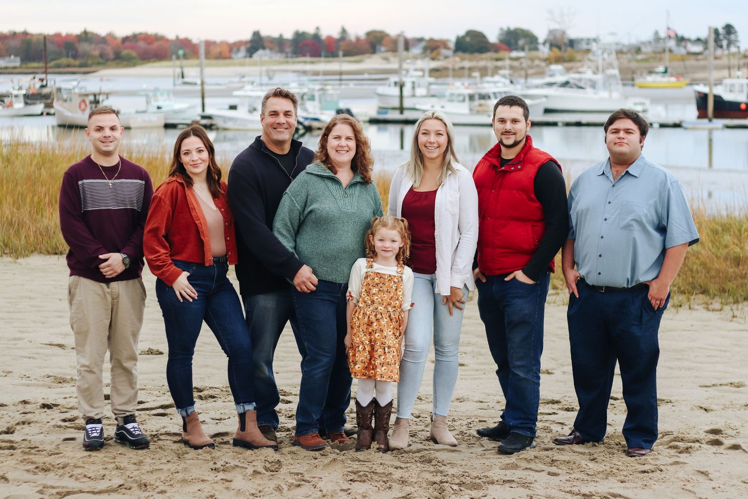 Group photo of family standing together on a beach with boats in the background.