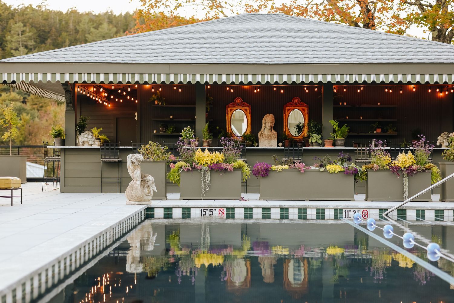 Outdoor swimming pool with string lights and autumn foliage visible in the surrounding trees and landscape.