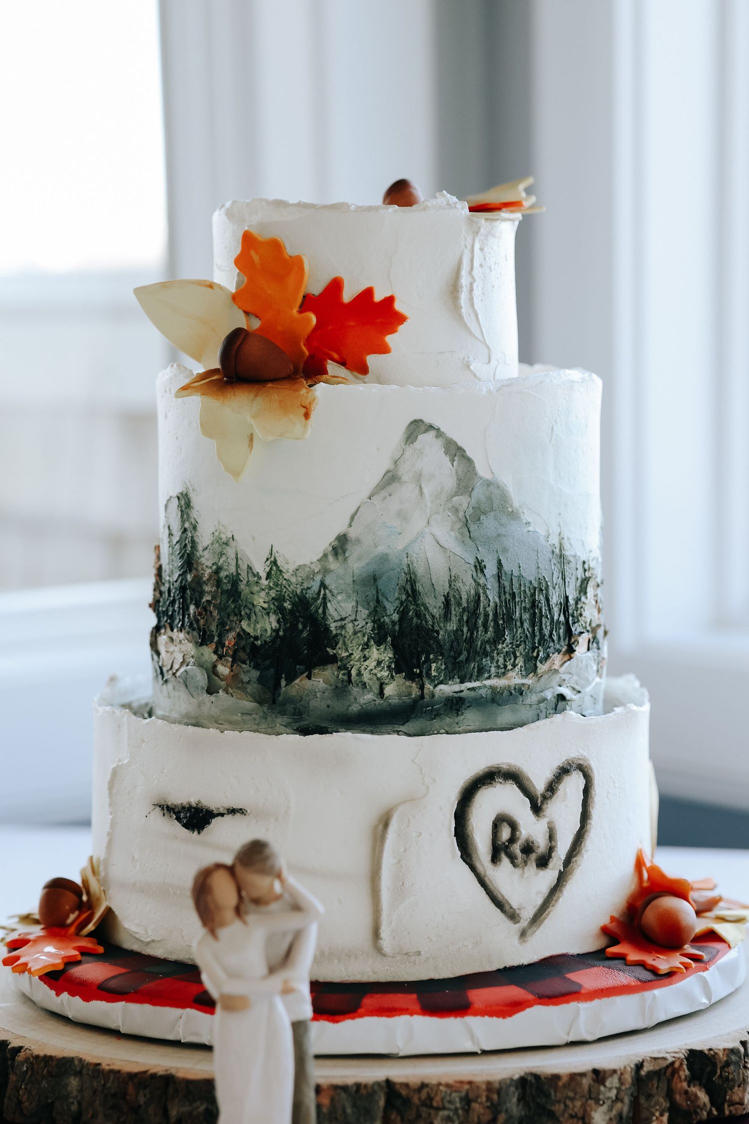 White wedding cake decorated with mountain landscape design and fall leaves on top displayed in multiple views.