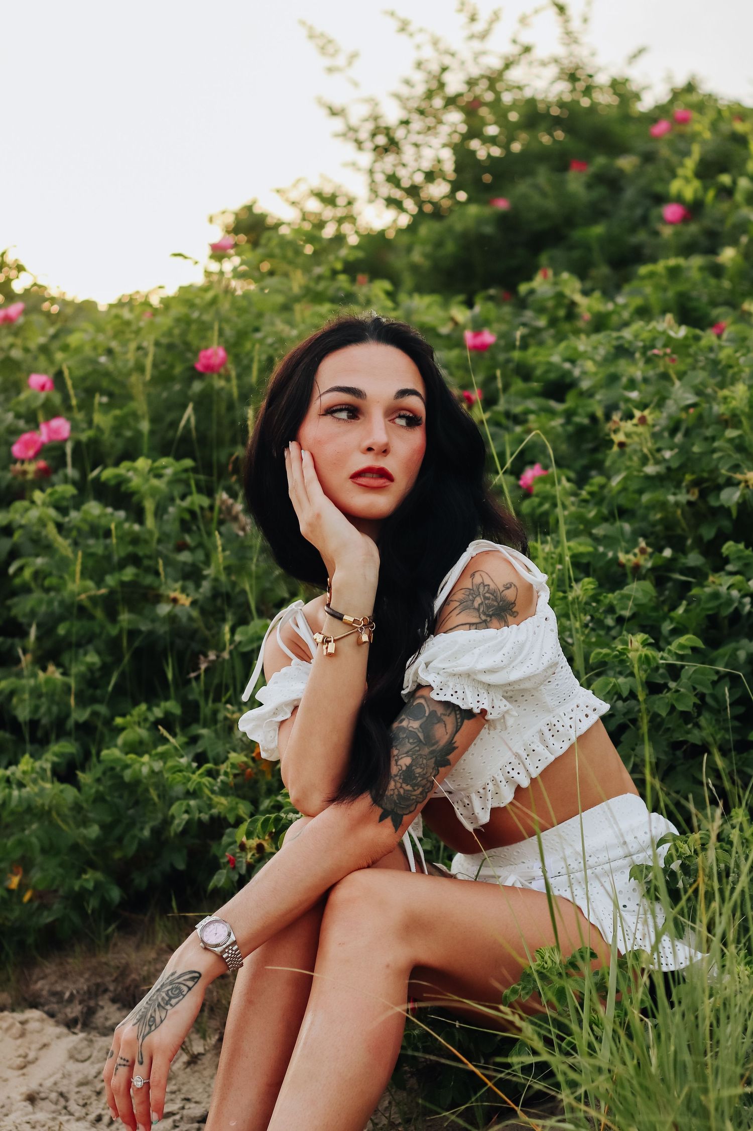 Solo female portrait in white dress sitting among pink beach roses at sunset.