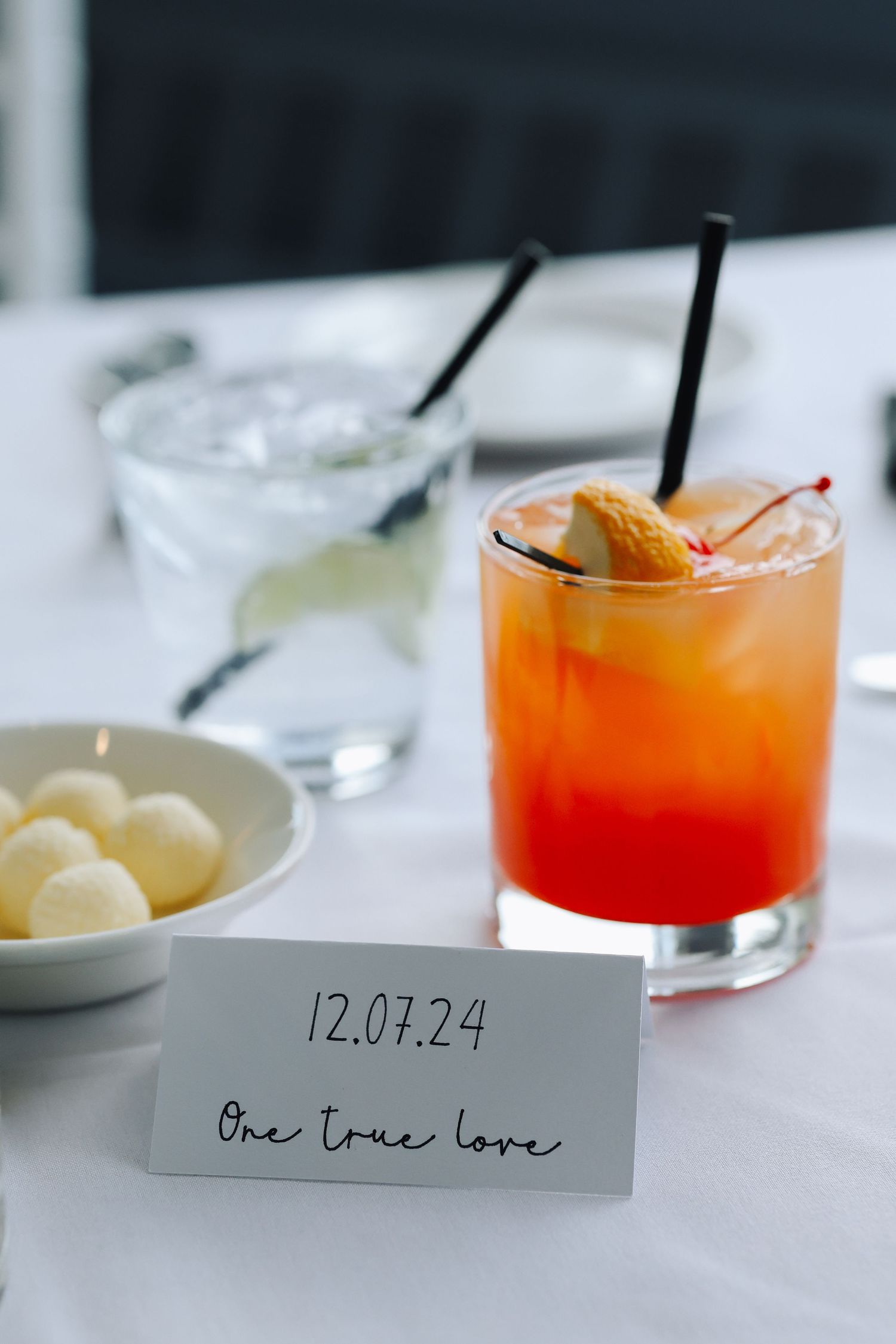 Orange cocktails with ice and citrus garnish served alongside place cards on a white tablecloth.